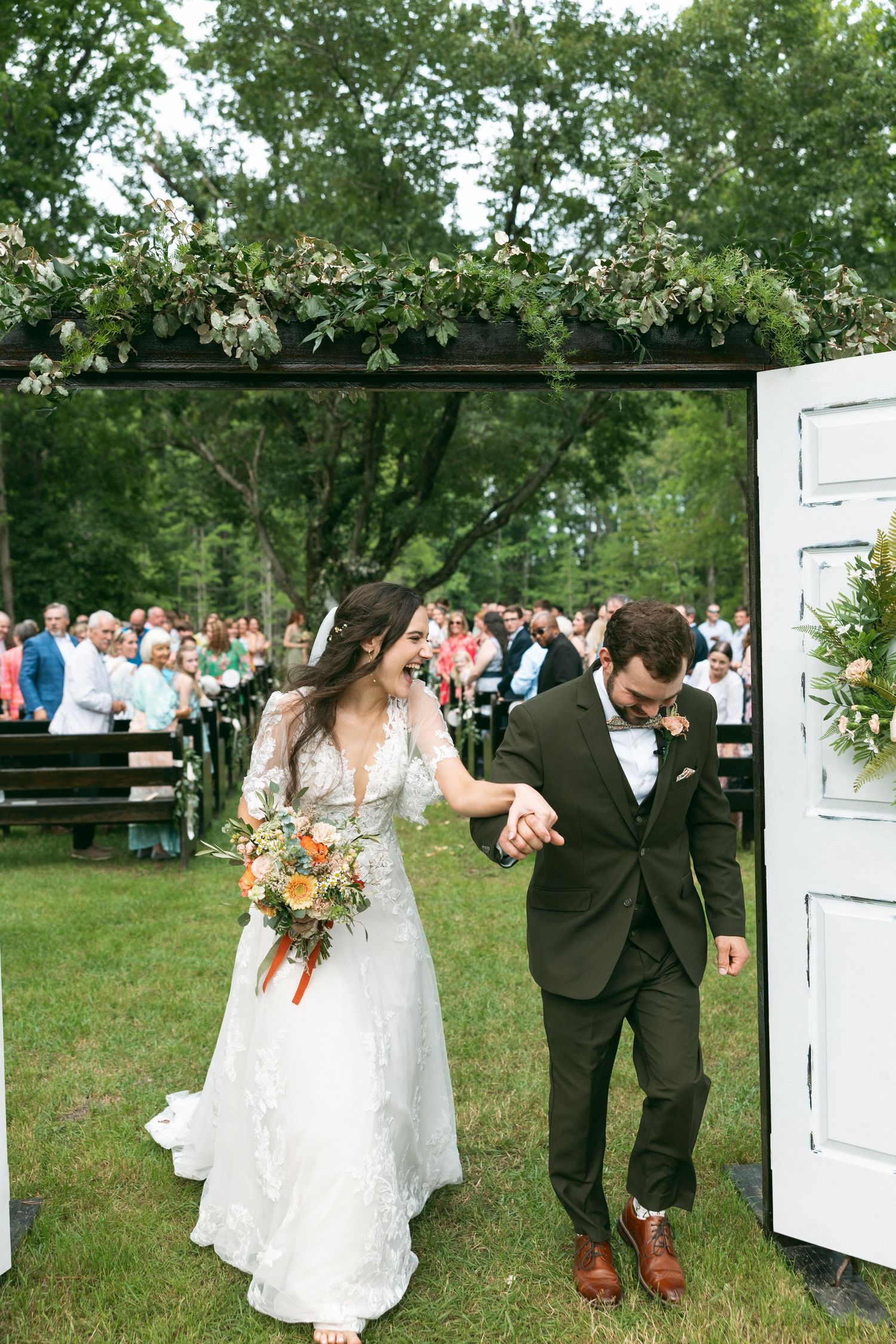 A celebratory exit through white doors after a wedding ceremony as guests cheer on the newlyweds in an outdoor garden.