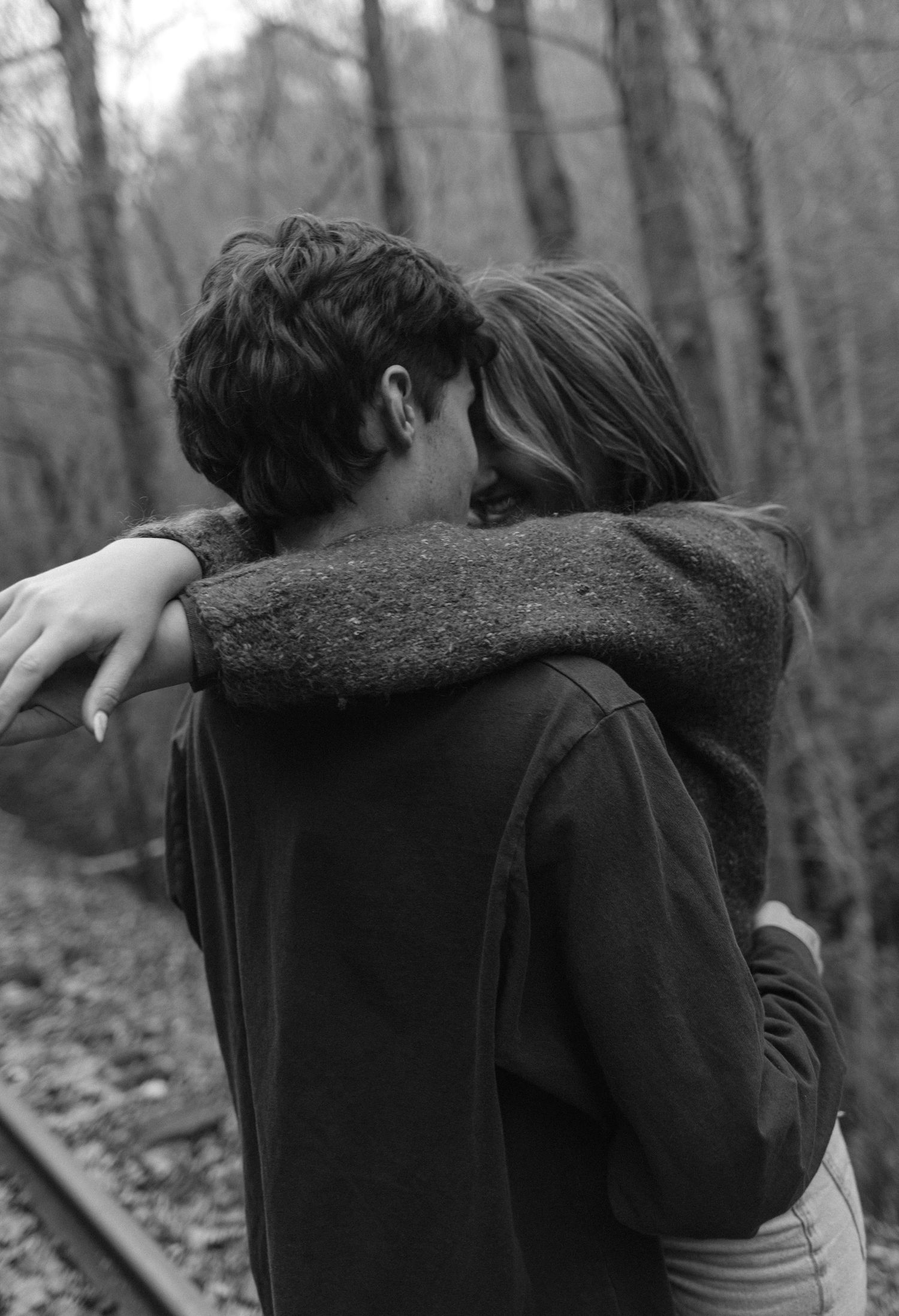 A tender black and white photograph of an intimate embrace between two people in a wooded forest setting.
