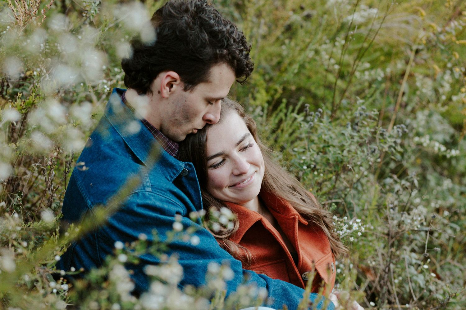 A couple sharing an intimate moment together outdoors among blooming wildflowers and greenery.