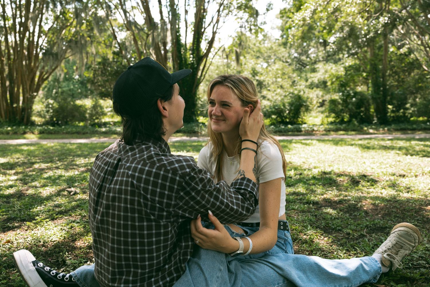 Two people share a tender moment while sitting together in a sunny park on a warm afternoon.