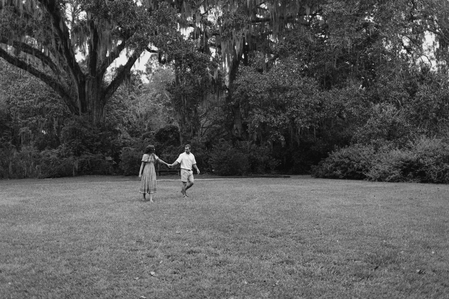 Two small children holding hands while walking together across a grassy field in a black and white photograph.