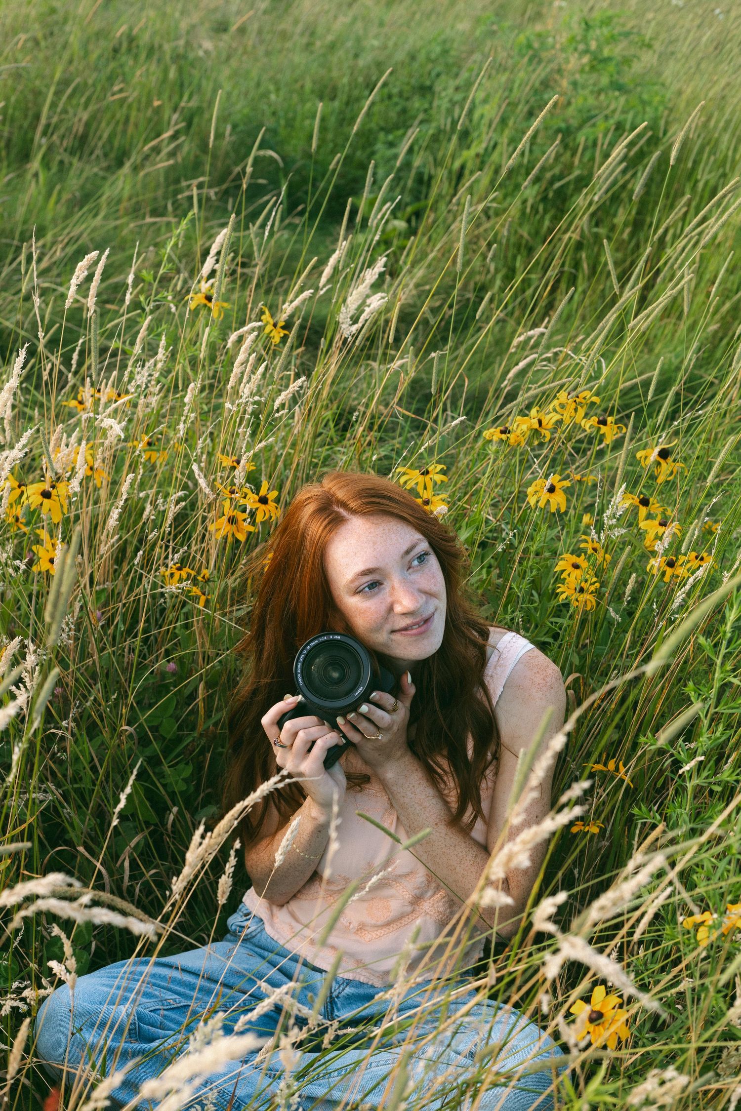 Person relaxing in a meadow with yellow wildflowers while holding a vintage camera in sunny weather.