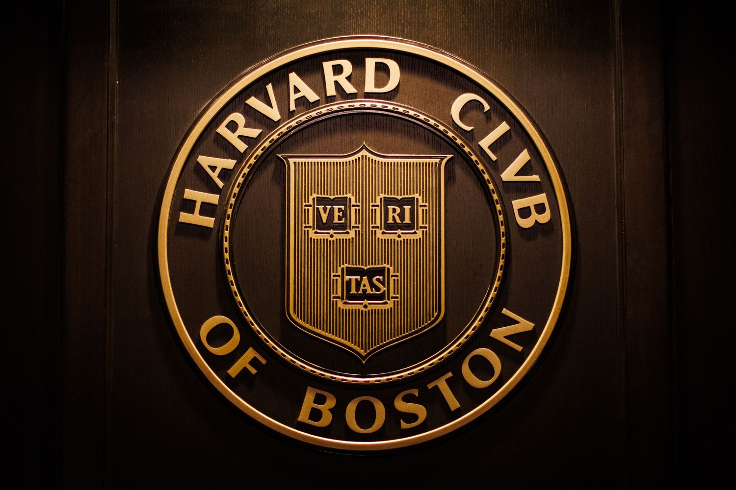 Harvard Club of Boston official gold emblem seal on wooden wall.