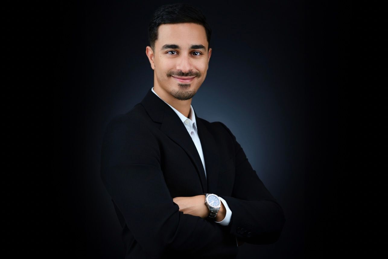 Confident professional man in black blazer with arms crossed against dark background.