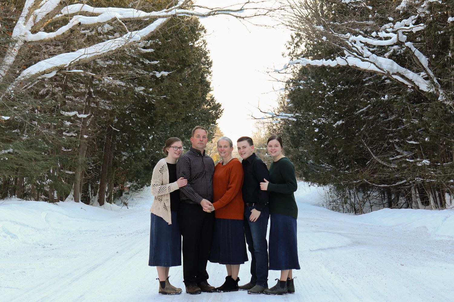 A group of people sitting on a bench in a snowy winter landscape surrounded by evergreen trees.