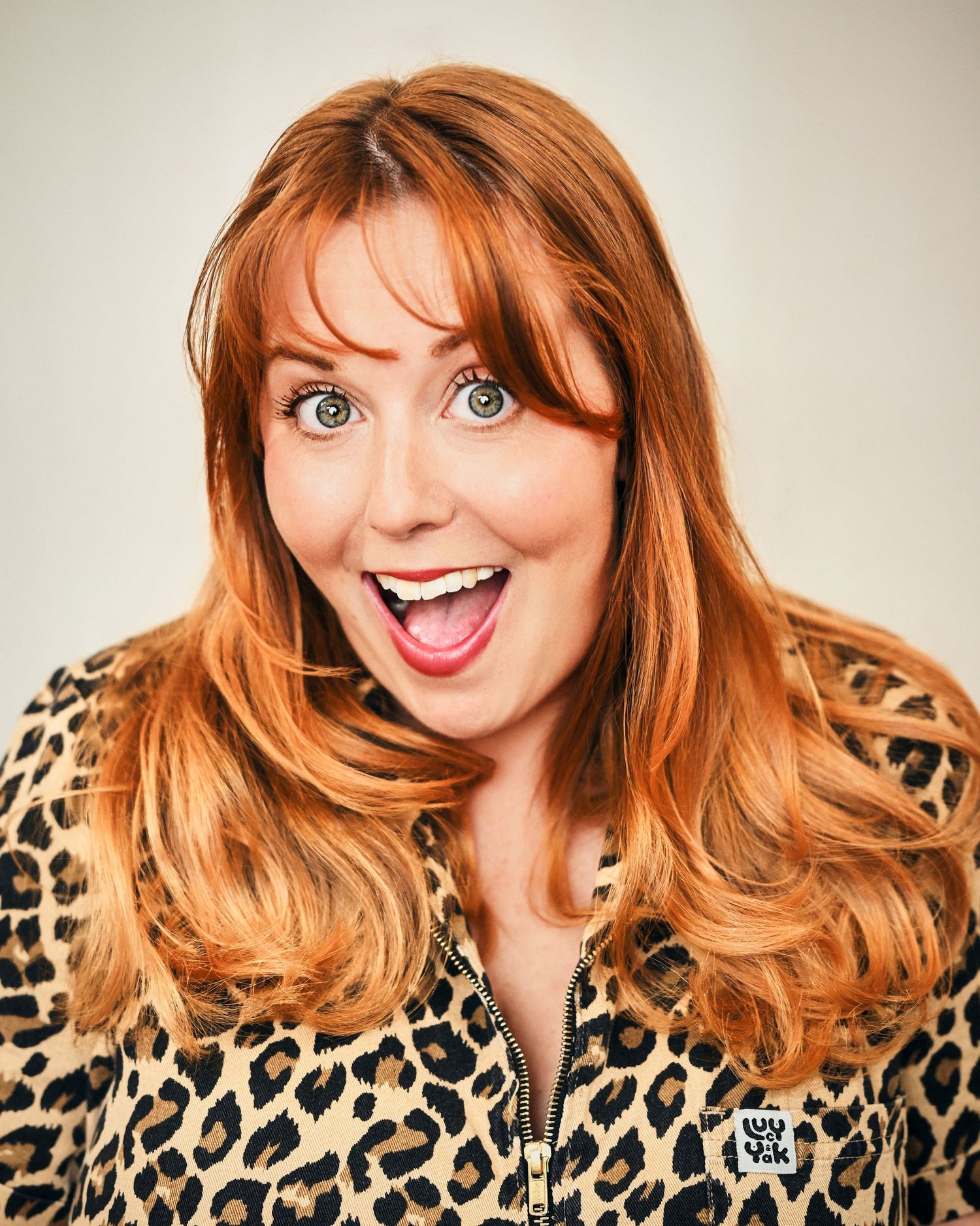 Smiling redhead woman in leopard print jacket with expressive blue eyes and open mouth expression.