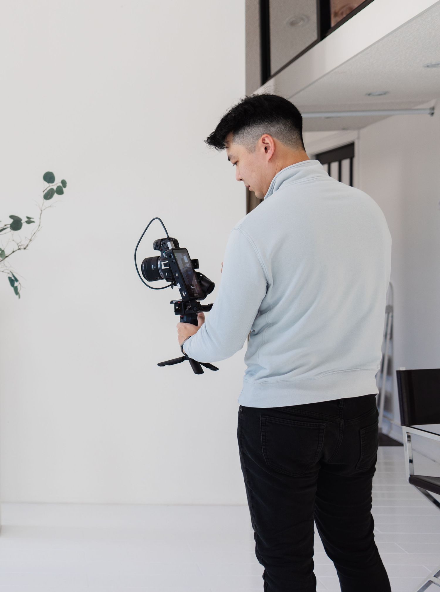Photographer setting up equipment in modern white studio space with plant decor.