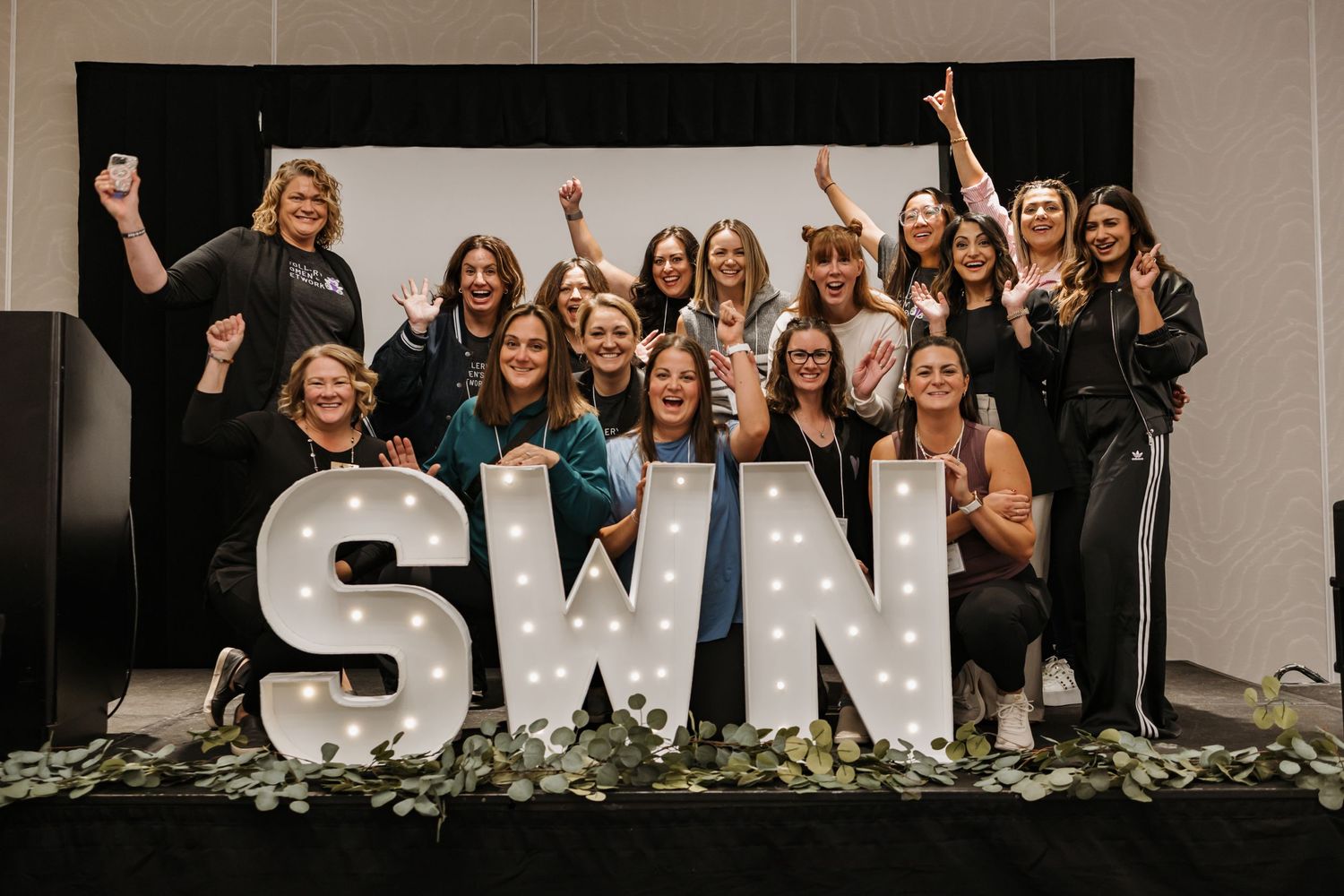 Group photo with illuminated SWN letters display and decorative greenery.