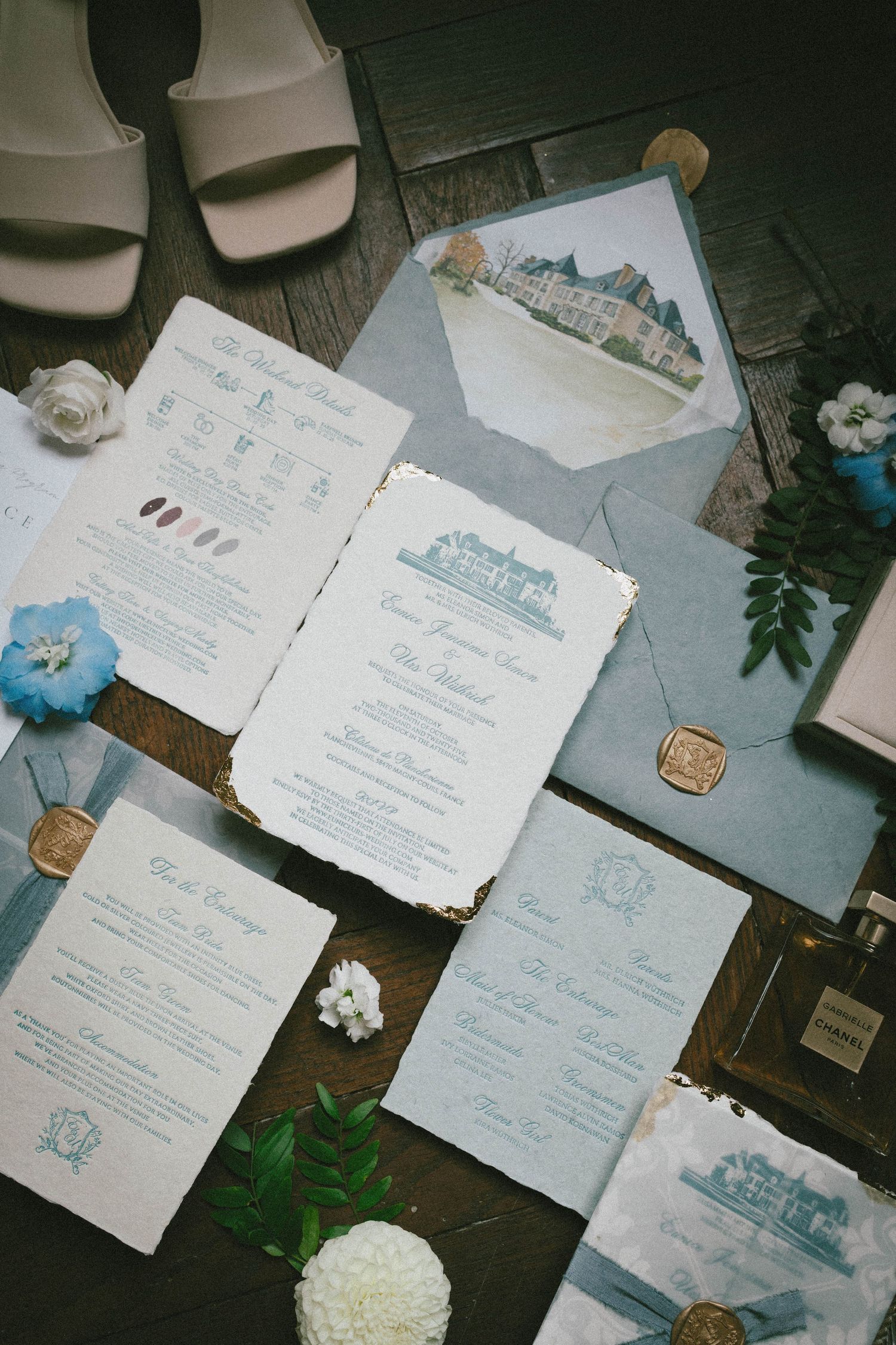 Wedding invitations and stationery with blue and gray color scheme laid out on dark wooden surface.