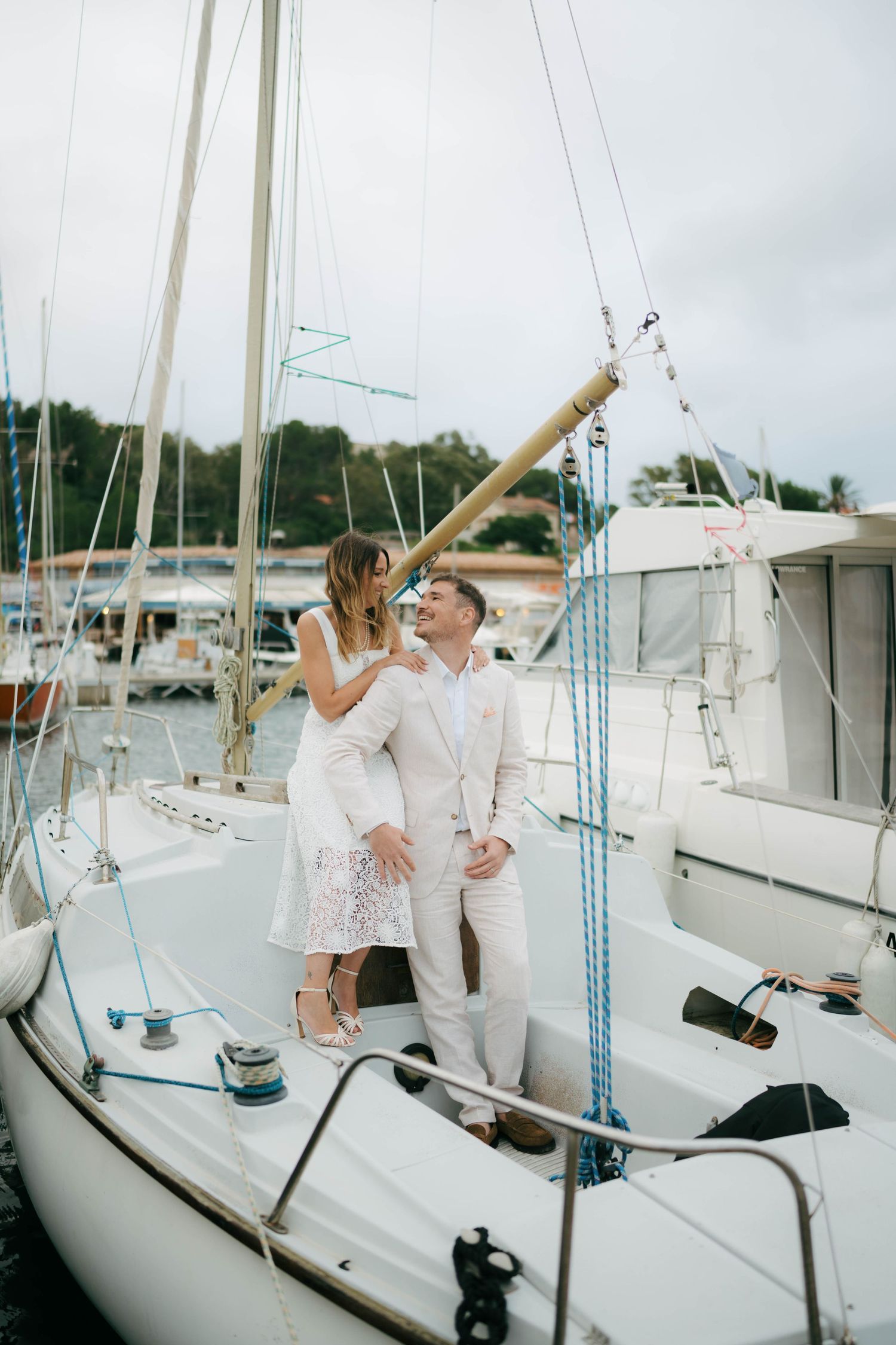 Couple celebrating with champagne on a white sailboat deck surrounded by nautical equipment and masts.