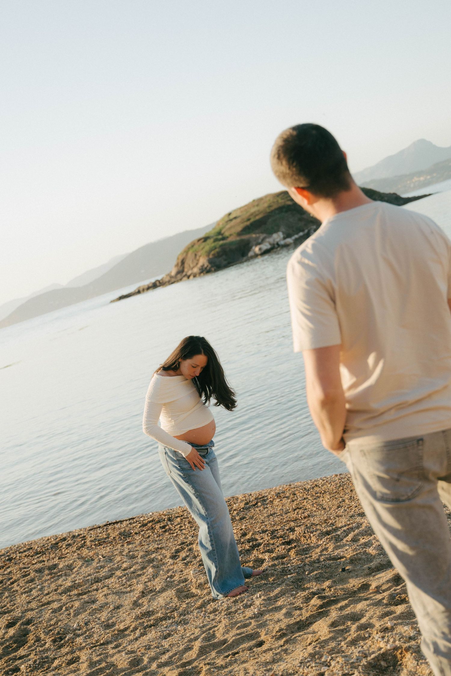 Un couple partage un moment ludique sur une plage pittoresque avec des montagnes et de l'eau en arrière-plan au coucher du soleil.