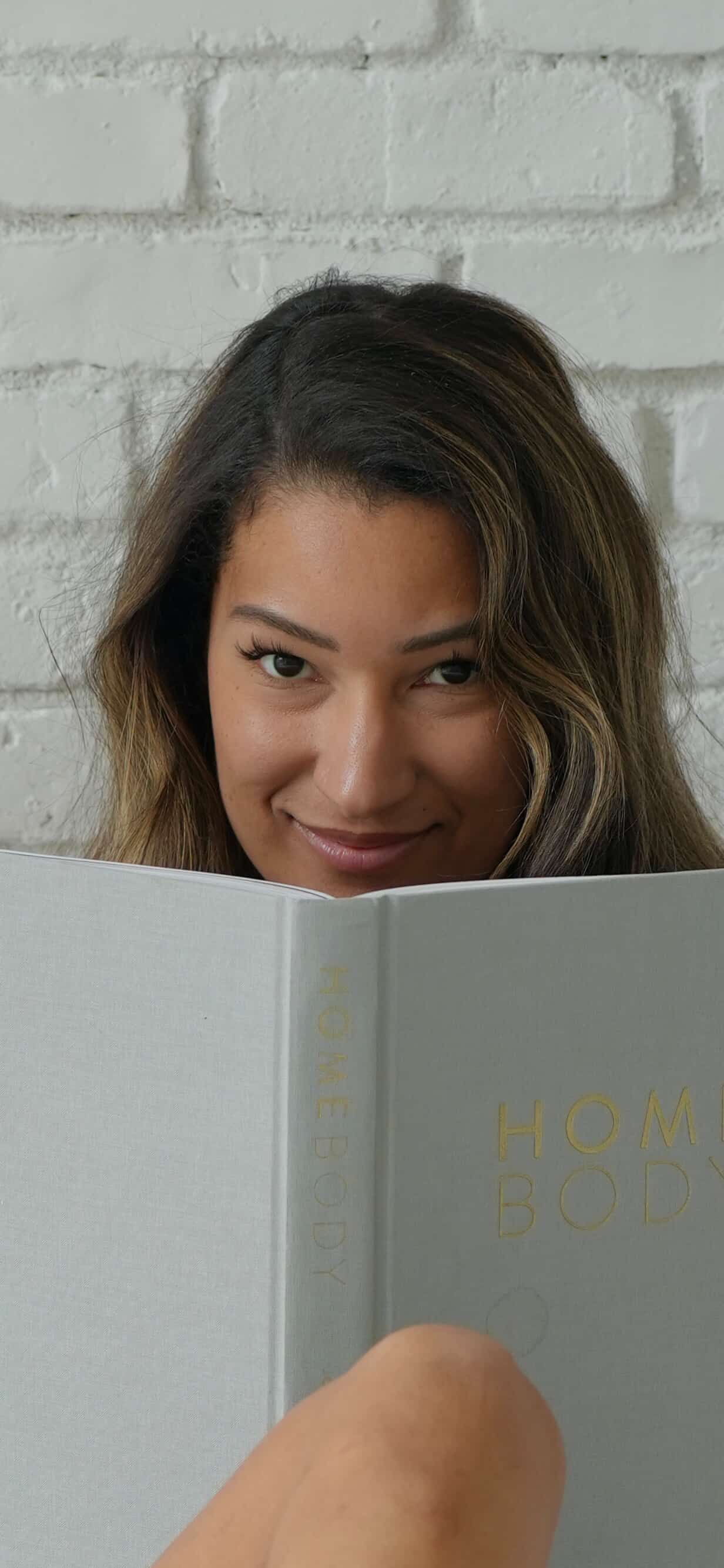 A series of three photos showing someone peeking playfully over a light gray book against a white brick wall background.