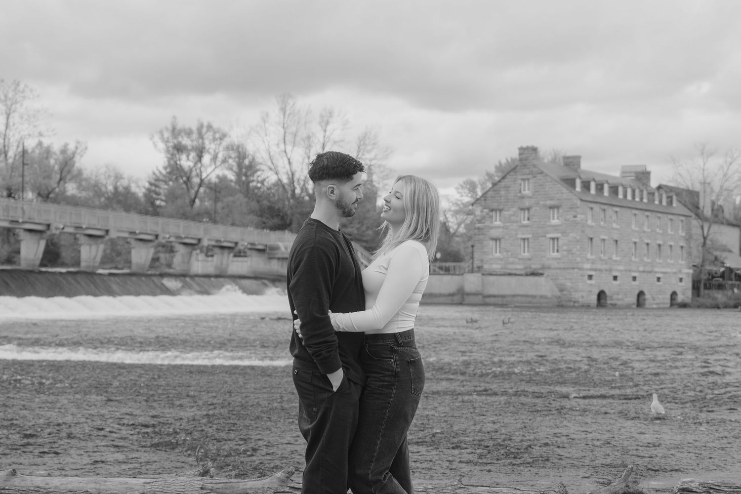 A romantic black and white scene of a couple embracing outdoors with an old stone building in the background.