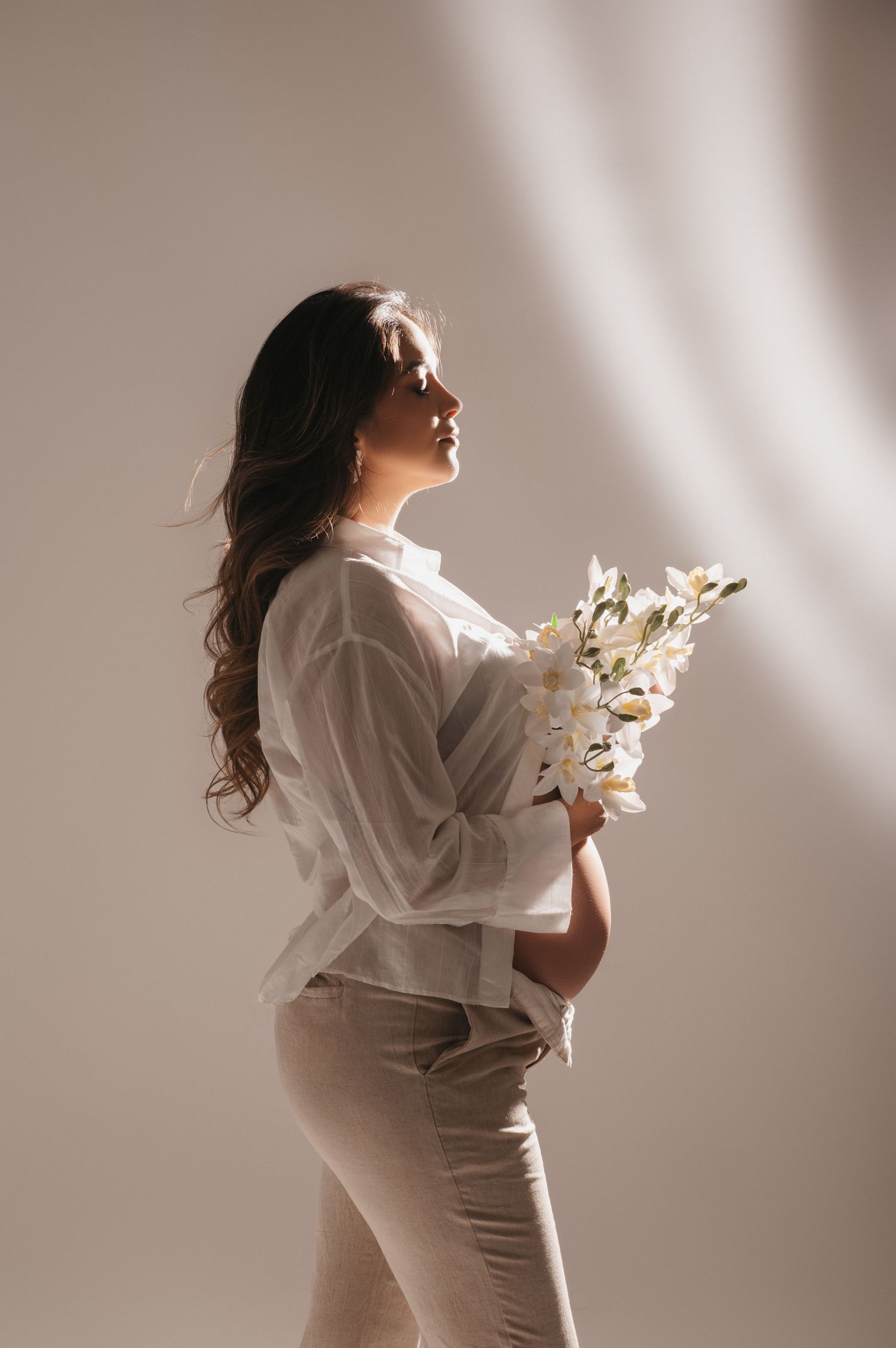 Ensaio de gestante em estúdio com gestante segurando flores e luz de recorte que ilumina a gestante