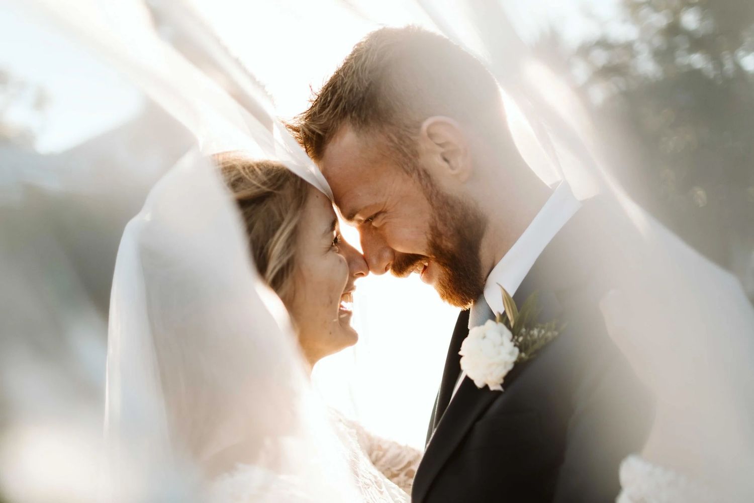A romantic wedding couple shares an intimate moment in soft sunlit lighting during their outdoor ceremony.