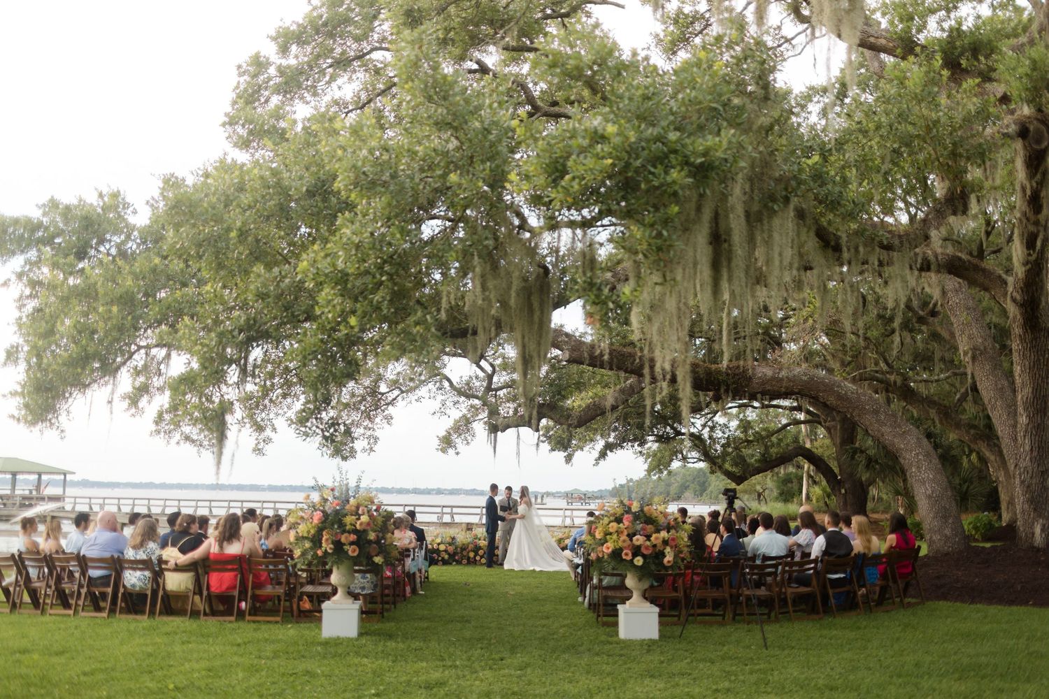 Wedding reception tables set under majestic oak trees draped with Spanish moss at an elegant outdoor venue.