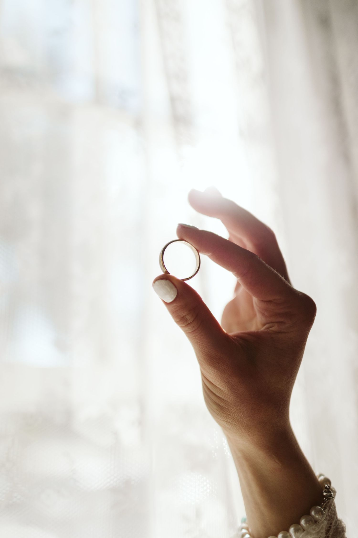 Hand holding up a small gold ring against a bright white background with soft lighting.
