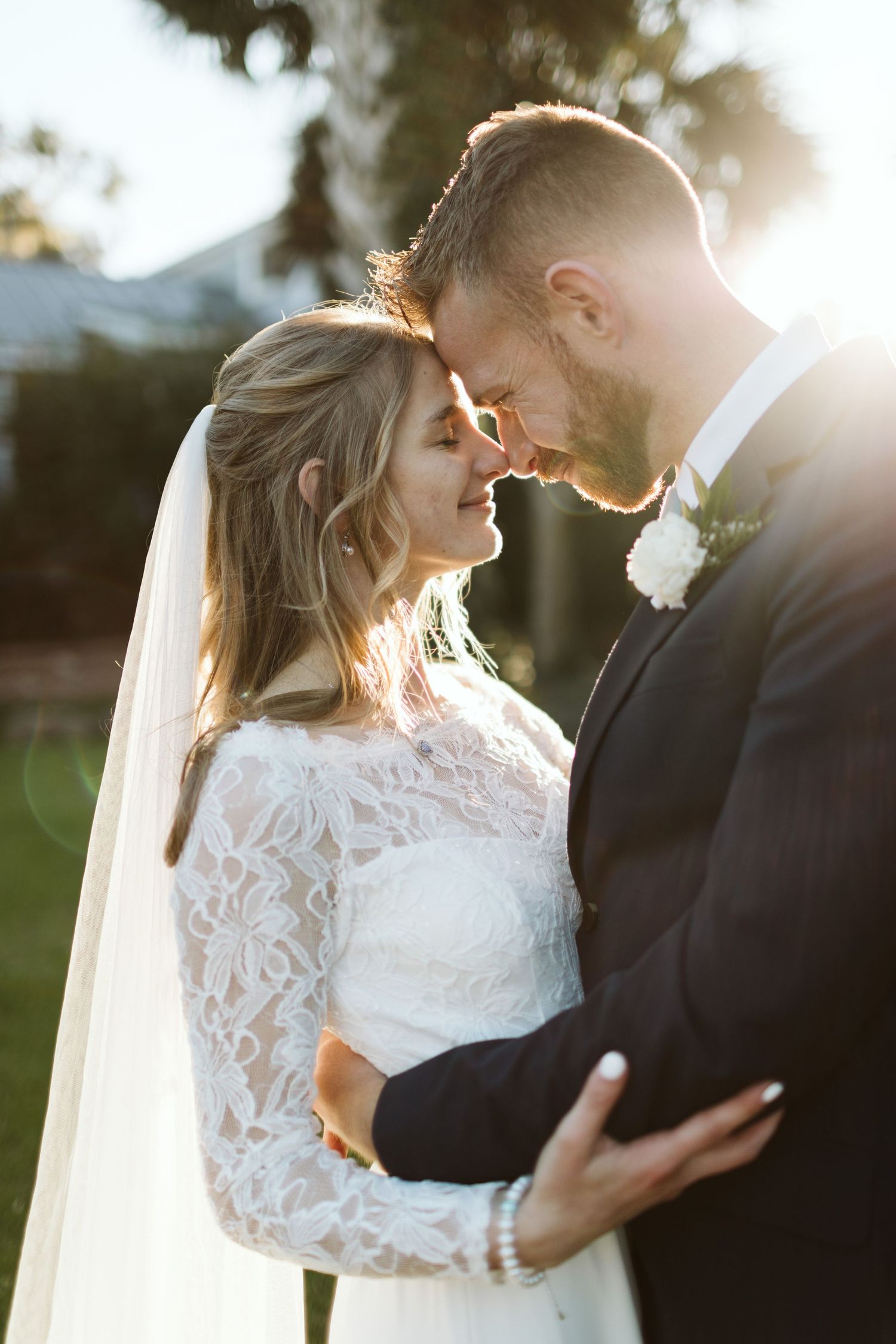 A romantic wedding couple embraces in golden sunlight while wearing traditional bridal attire and veil.