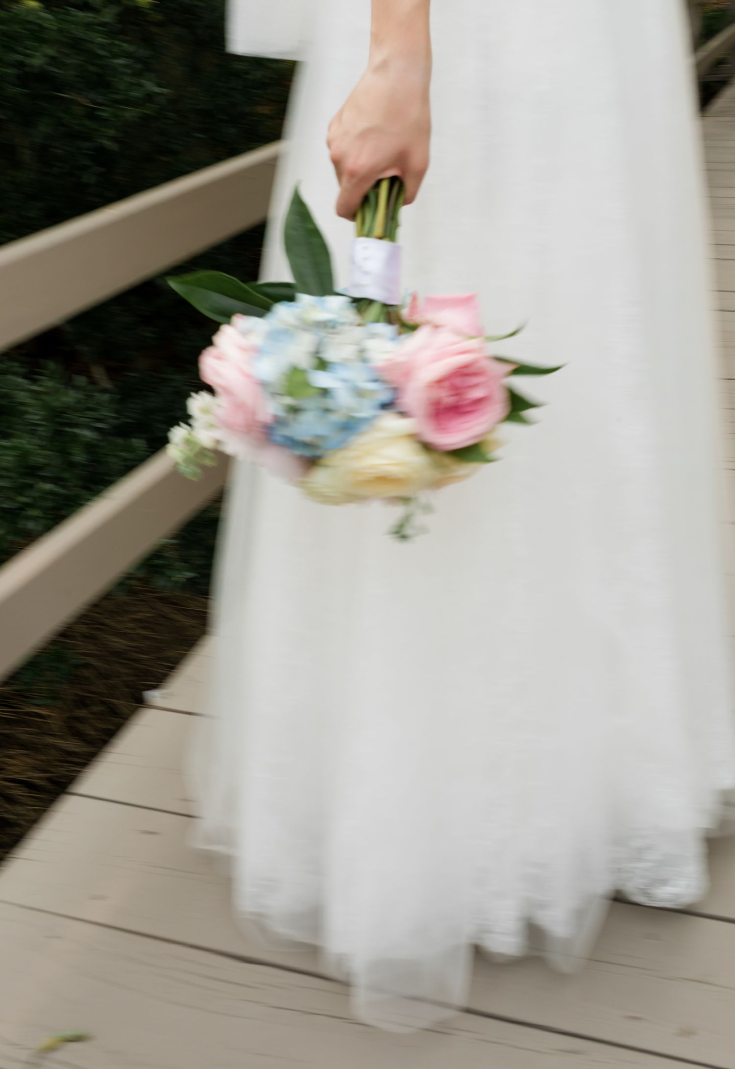 A blurred motion shot of a white wedding dress and pastel bouquet with pink and blue flowers.