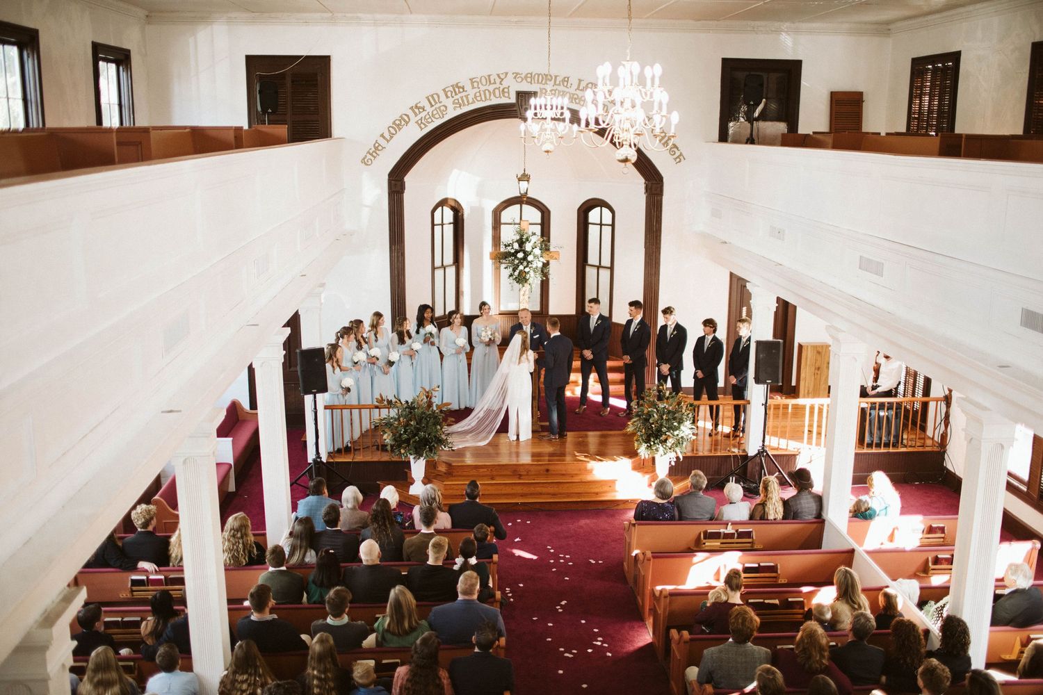 Wedding ceremony taking place in a traditional church sanctuary with wooden pews and white decor.