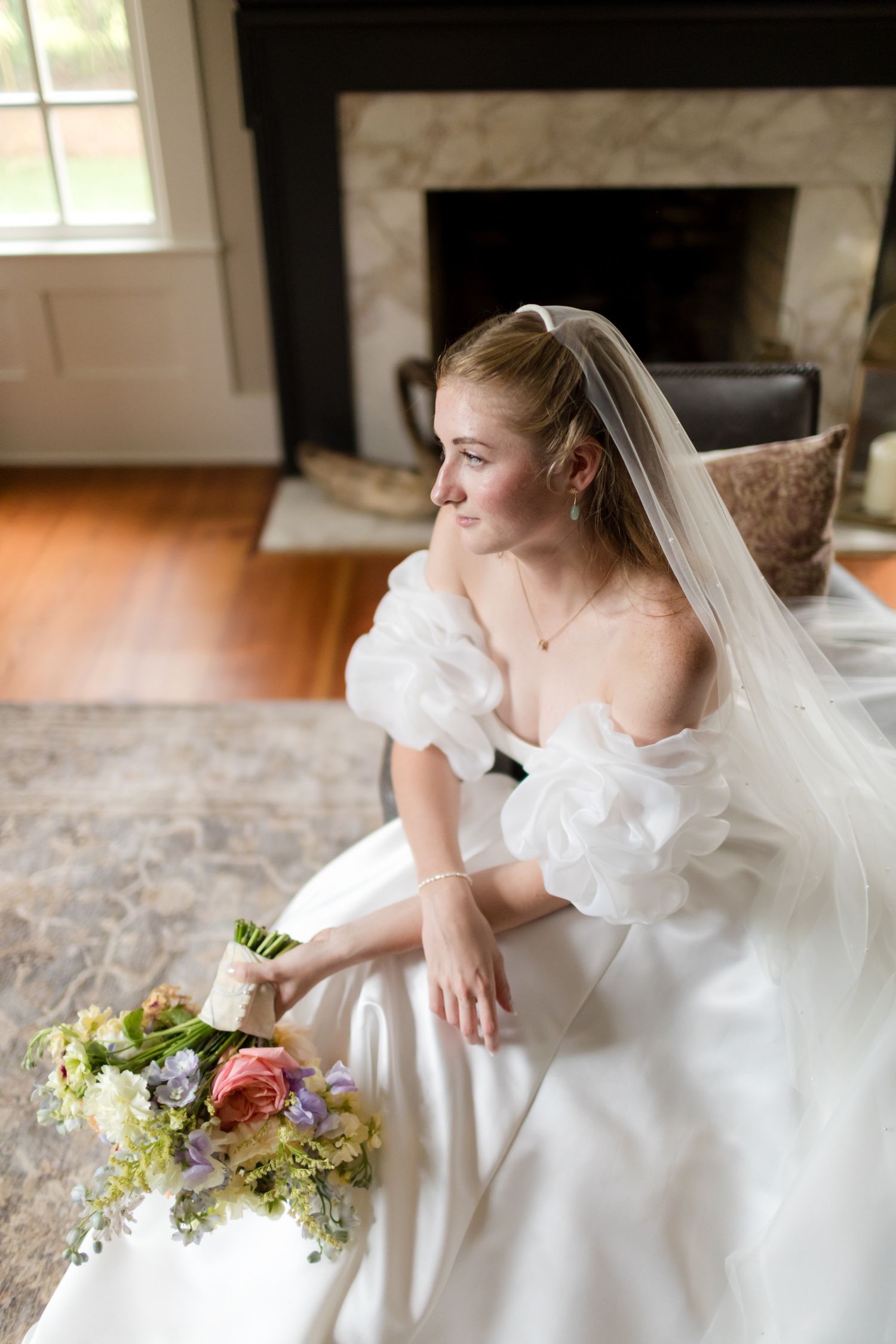 A bride in a white gown and veil sits gracefully while holding a colorful bouquet of flowers.