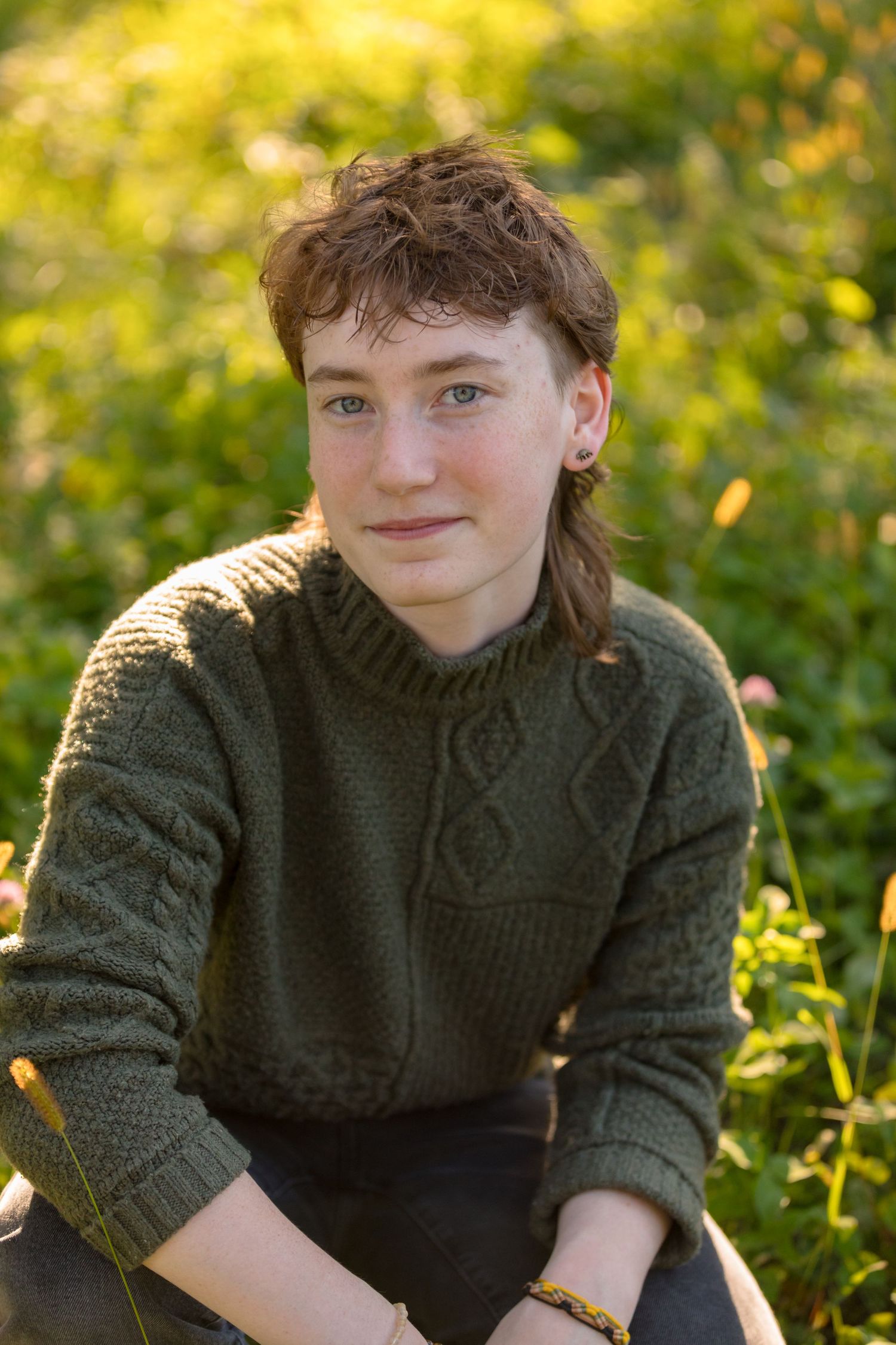 Musician wearing green cable knit sweater seated in sunny garden setting.