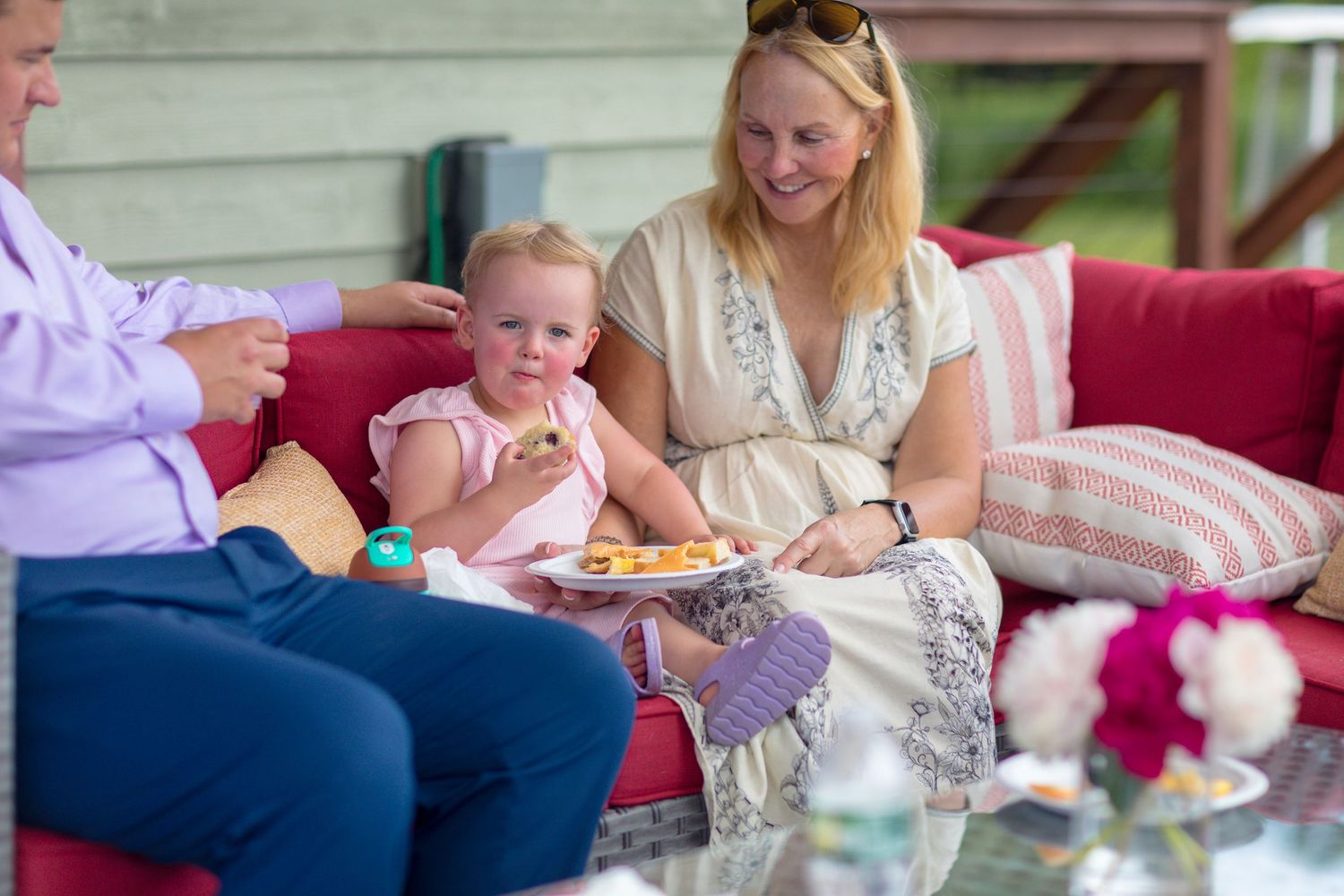 Family gathering around a table with food and drinks on a covered patio.