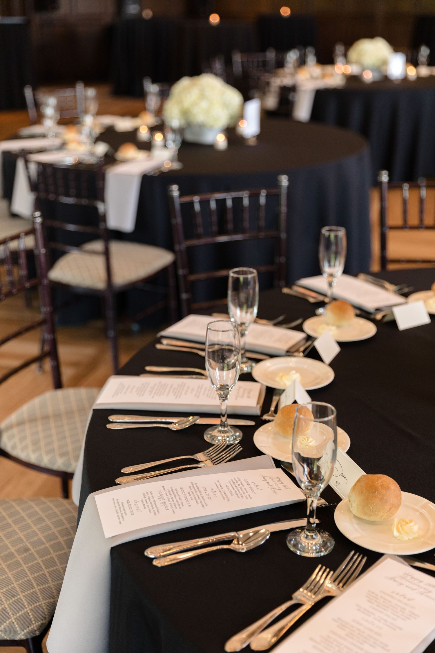 Formal table settings with black linens, menus and place settings at an event venue.