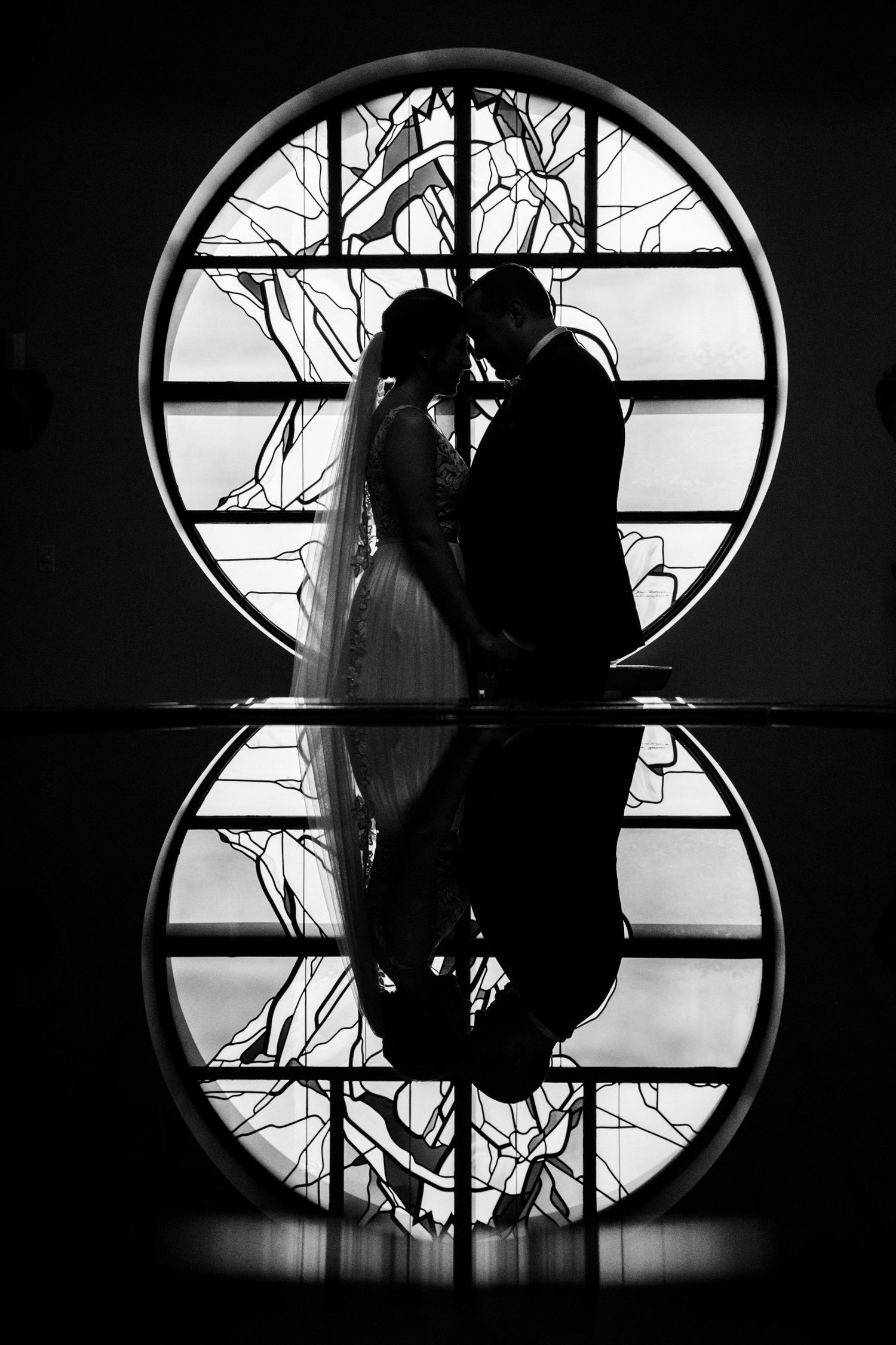A silhouetted couple in wedding attire against a circular window creating a dramatic reflection.