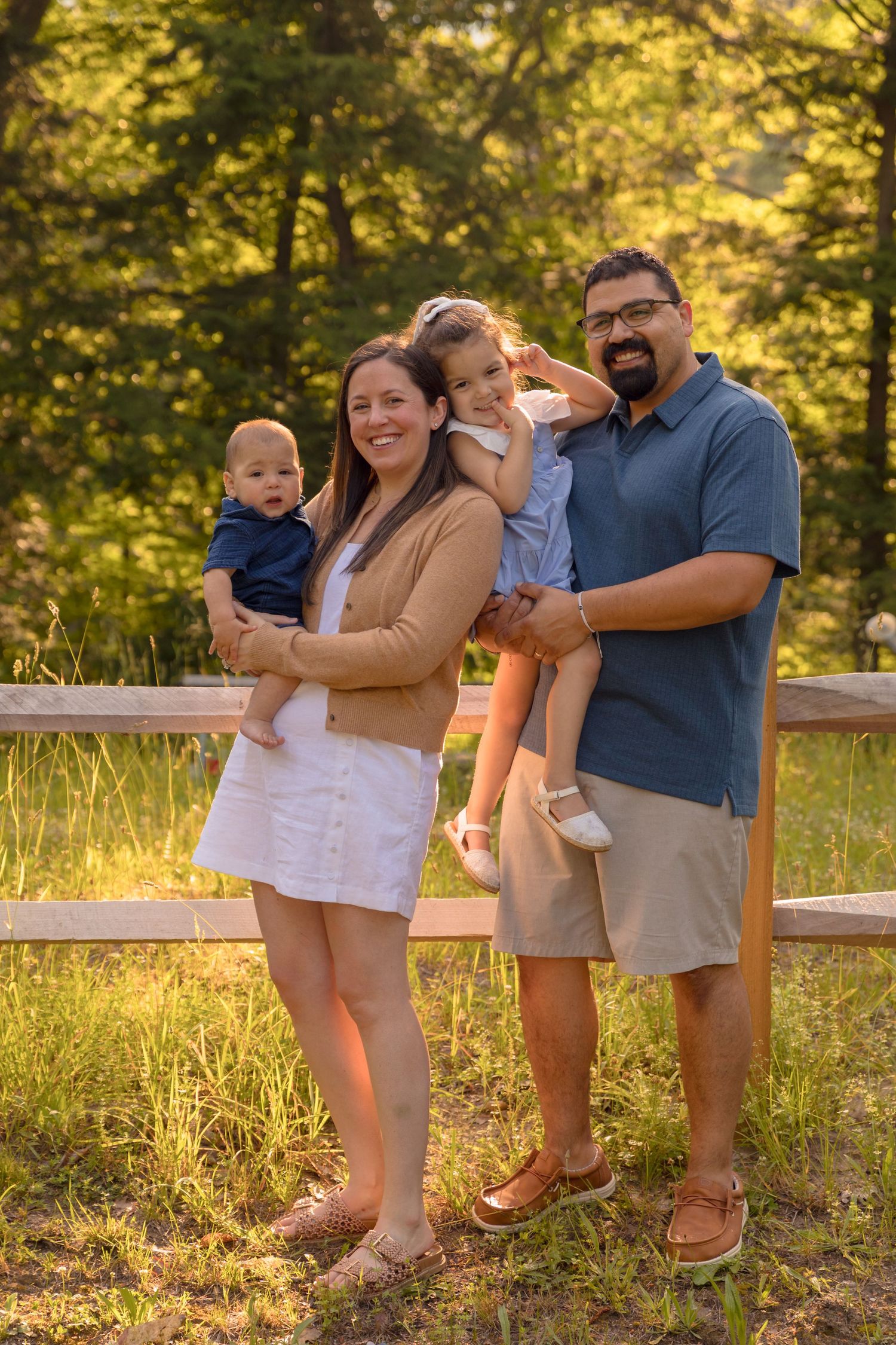 Family posing together by wooden fence during golden hour photo session.