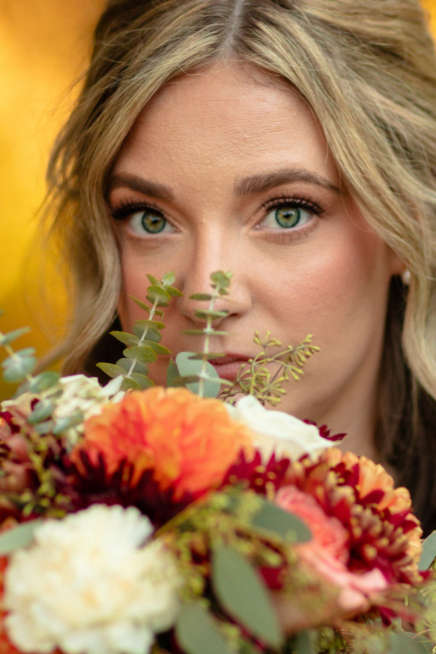 Close-up artistic shot of eyes peeking over a colorful autumn wedding bouquet.