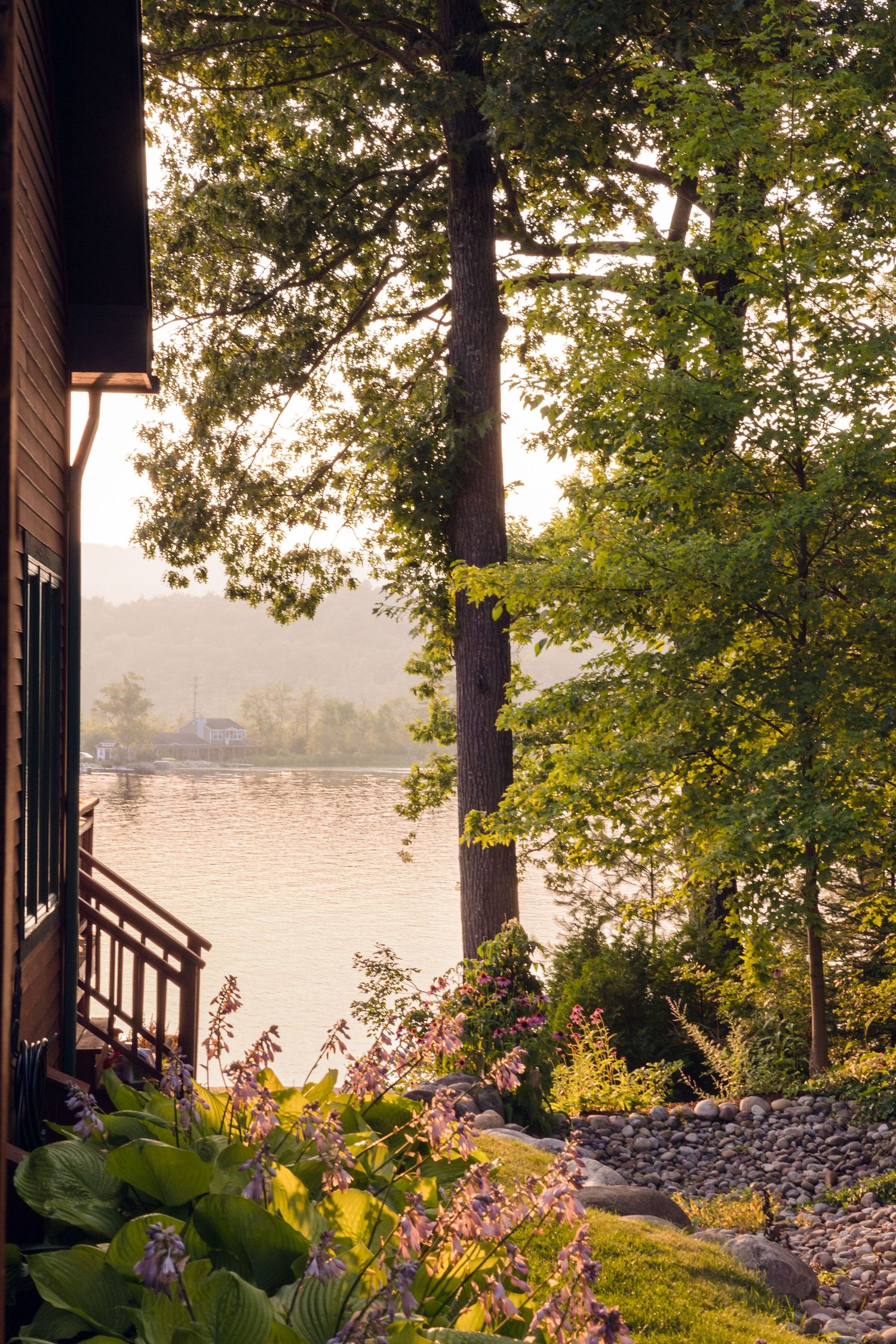 Scenic lakeside view with flowers and trees at sunset through cabin window.