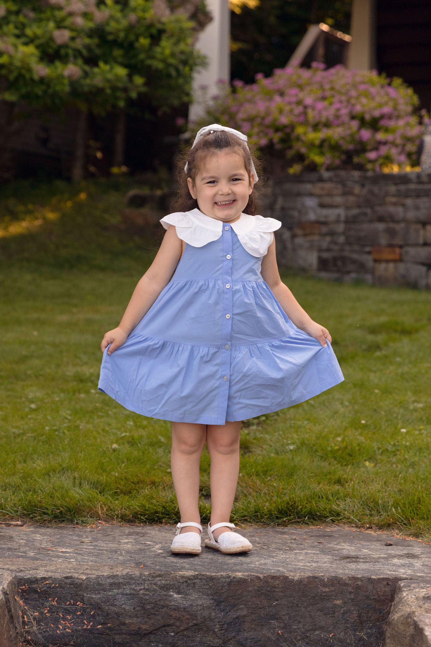 Child in blue dress twirling on stone wall during outdoor photo session.