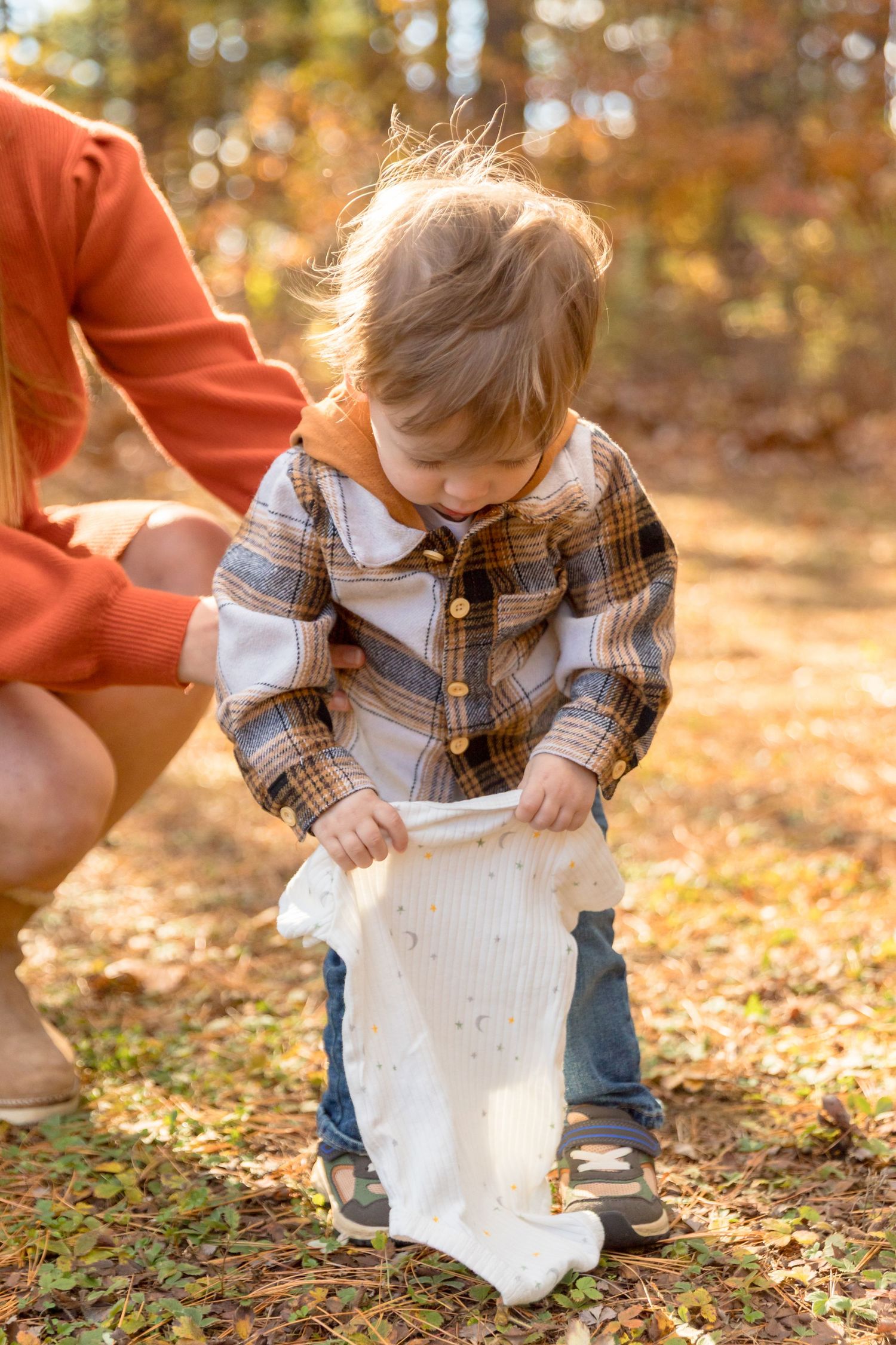 Small child explores fallen leaves during autumn family photo session in the woods.