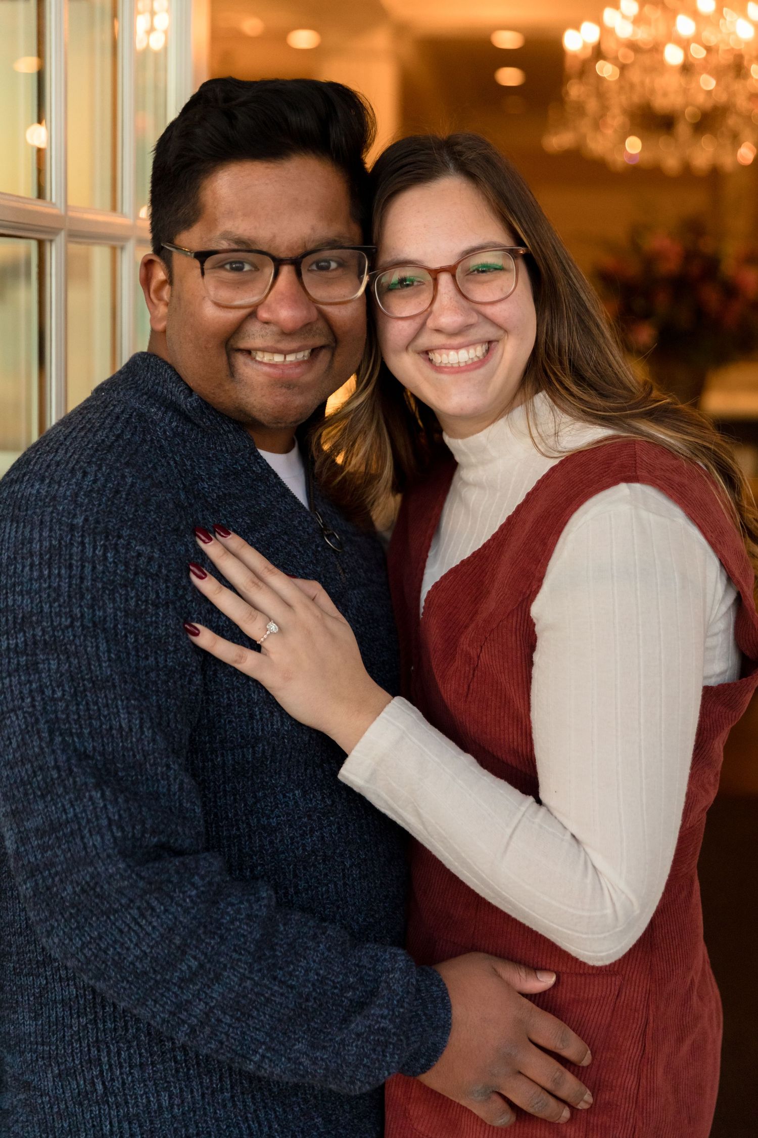 Indoor engagement photo with couple embracing under warm chandelier lighting.
