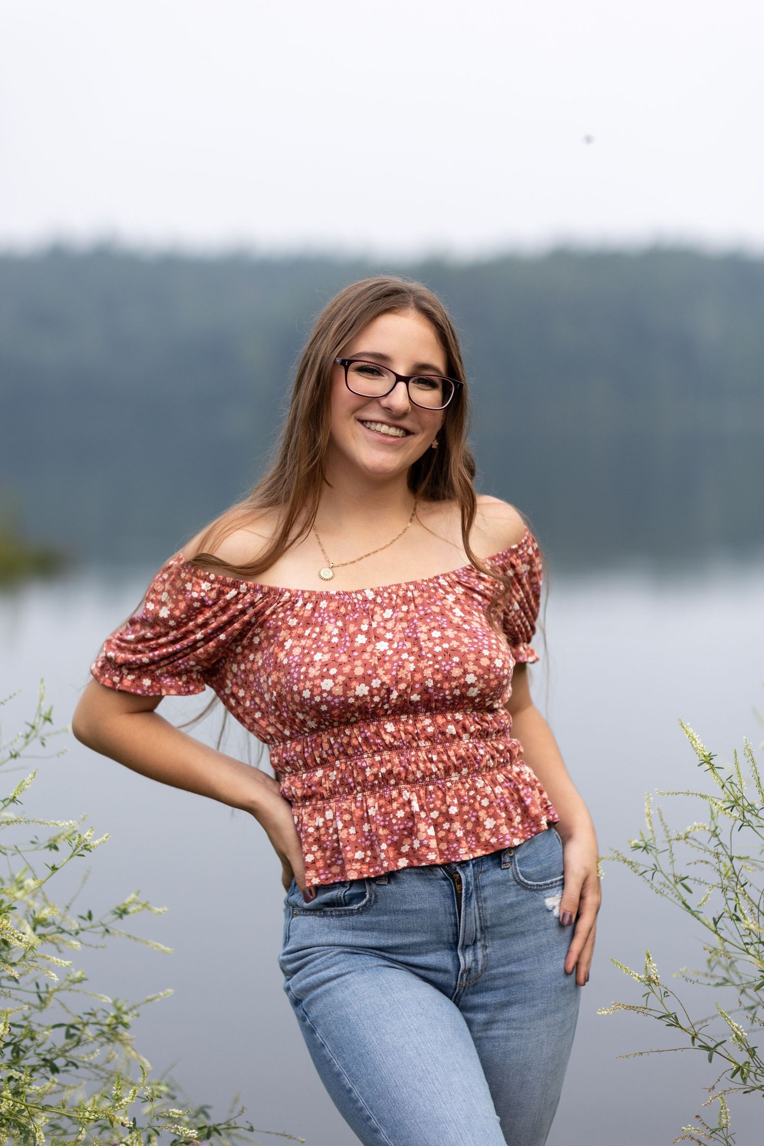 A floral crop top and blue jeans outfit photographed against a serene lake backdrop.