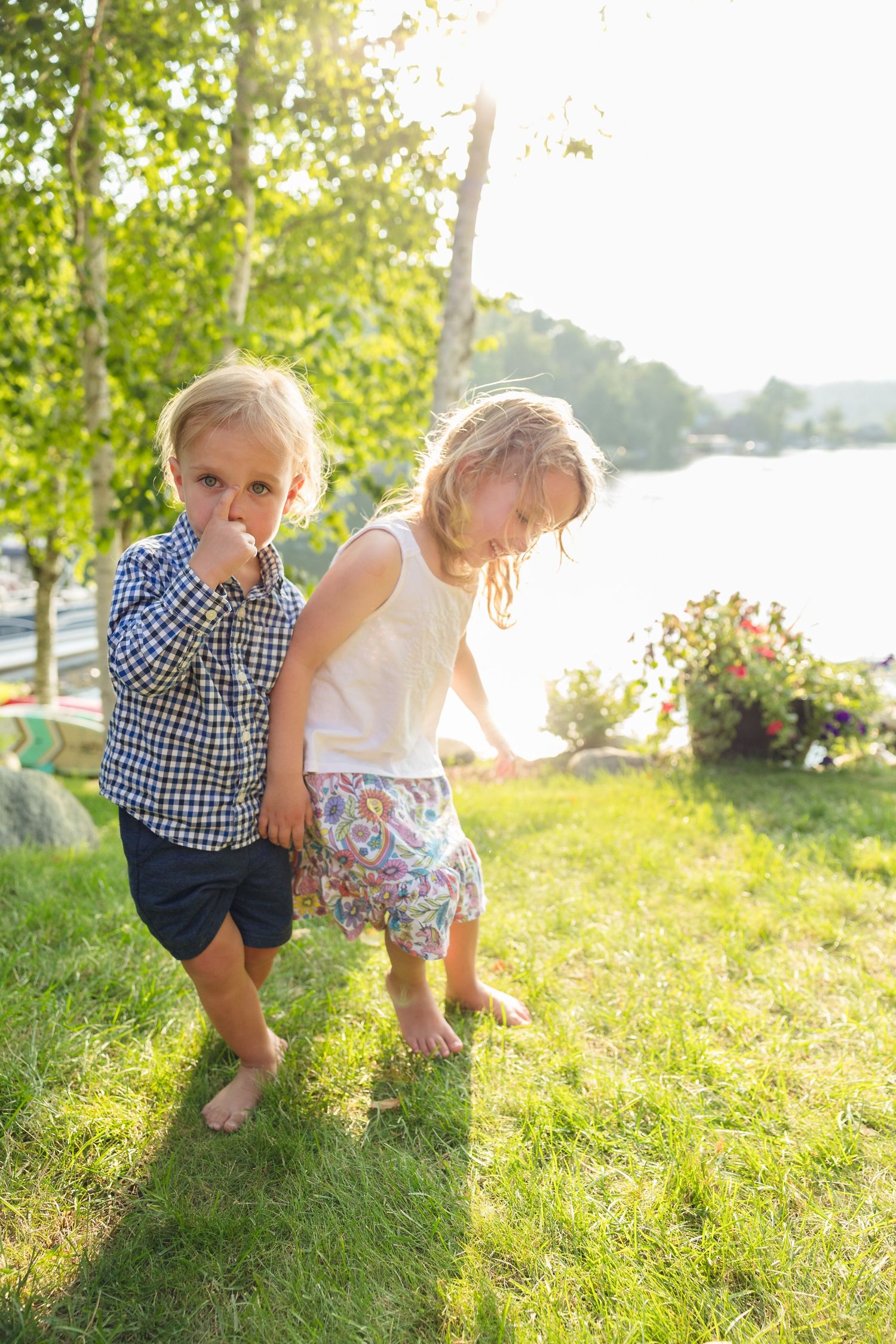 Two children playing together on grass near a lake during golden hour.