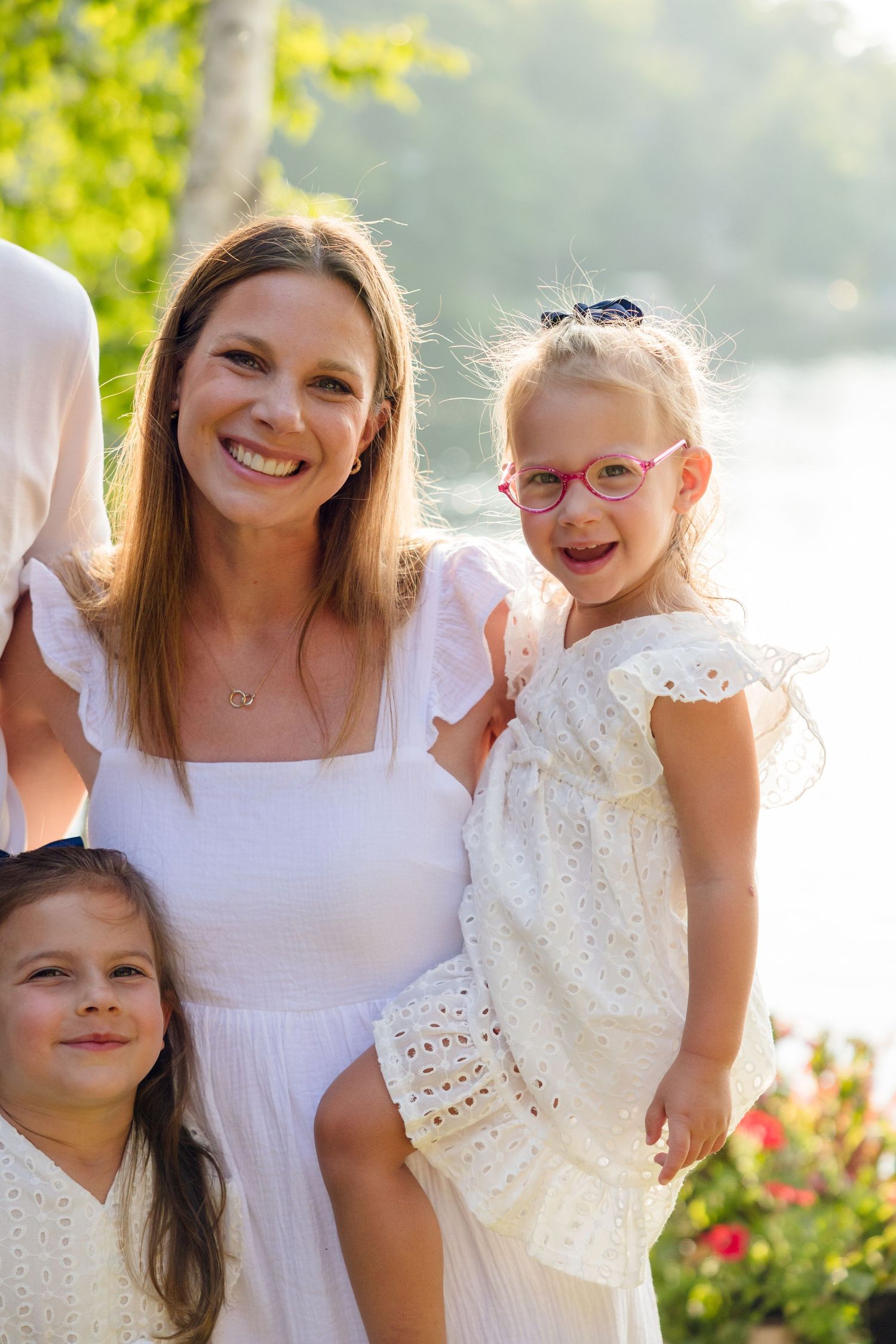 Happy family members in white clothing pose together against a sunlit natural background.