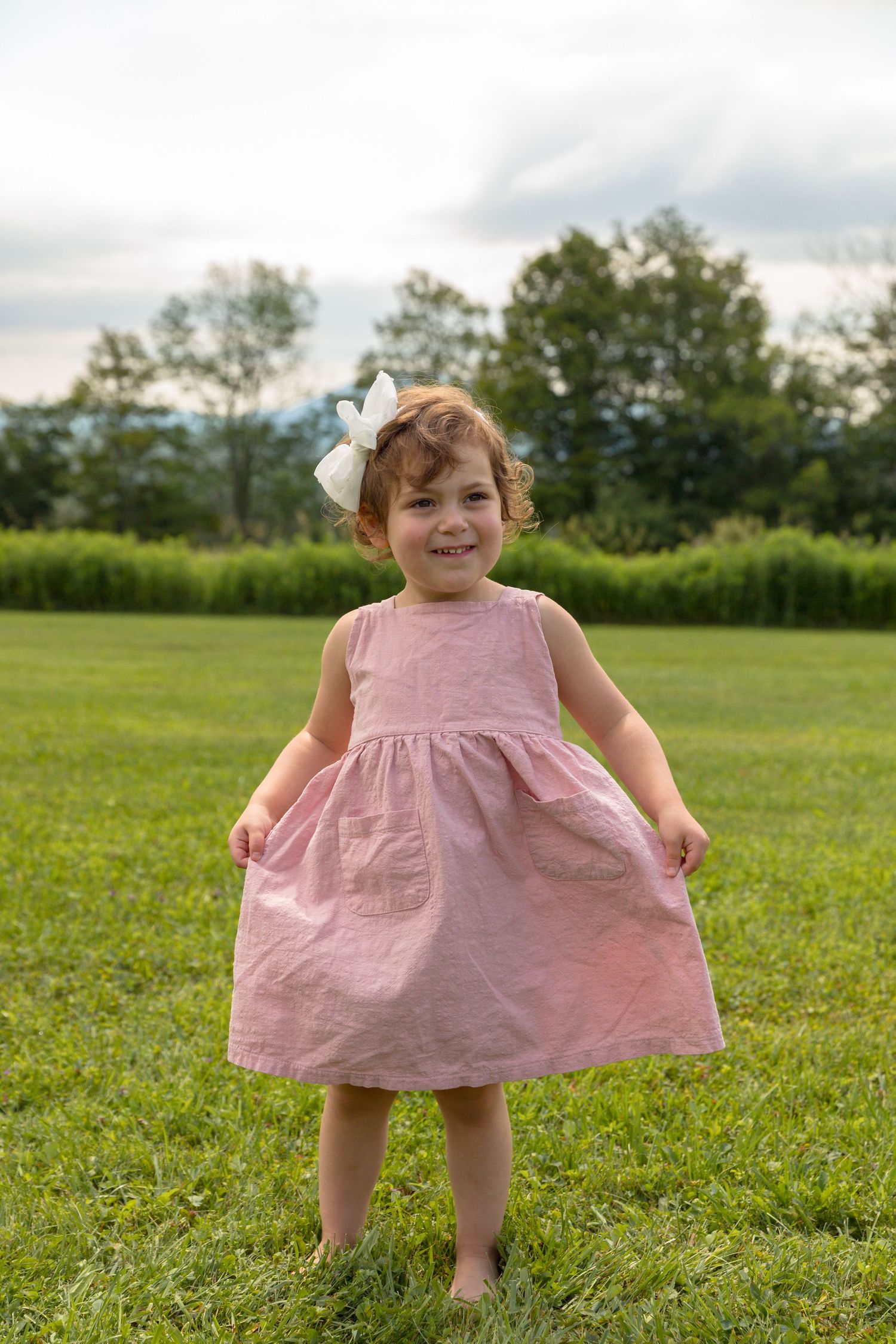 Young child in pink dress twirls playfully in a sunny green field.