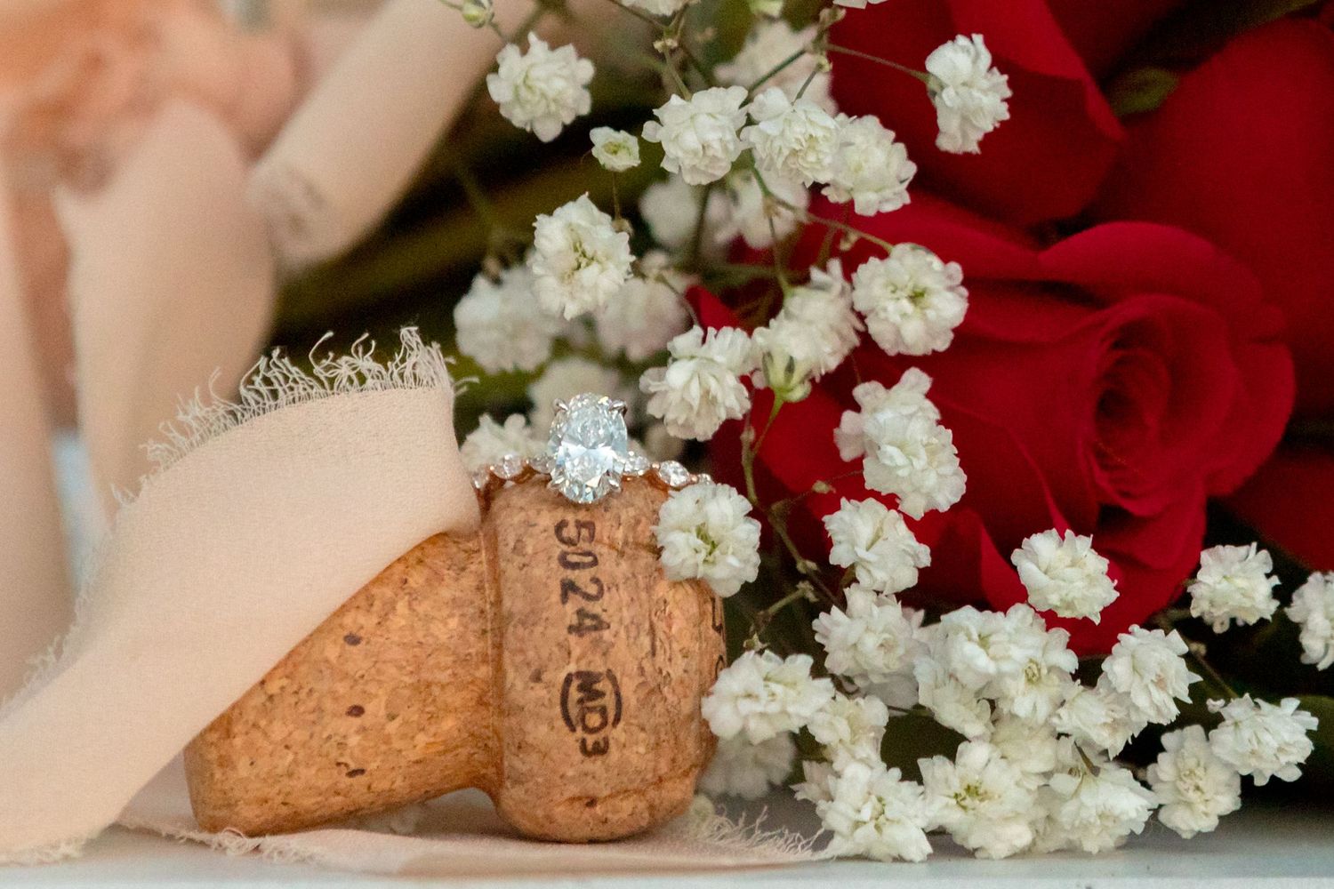 White flowers and champagne corks arranged on red velvet fabric.