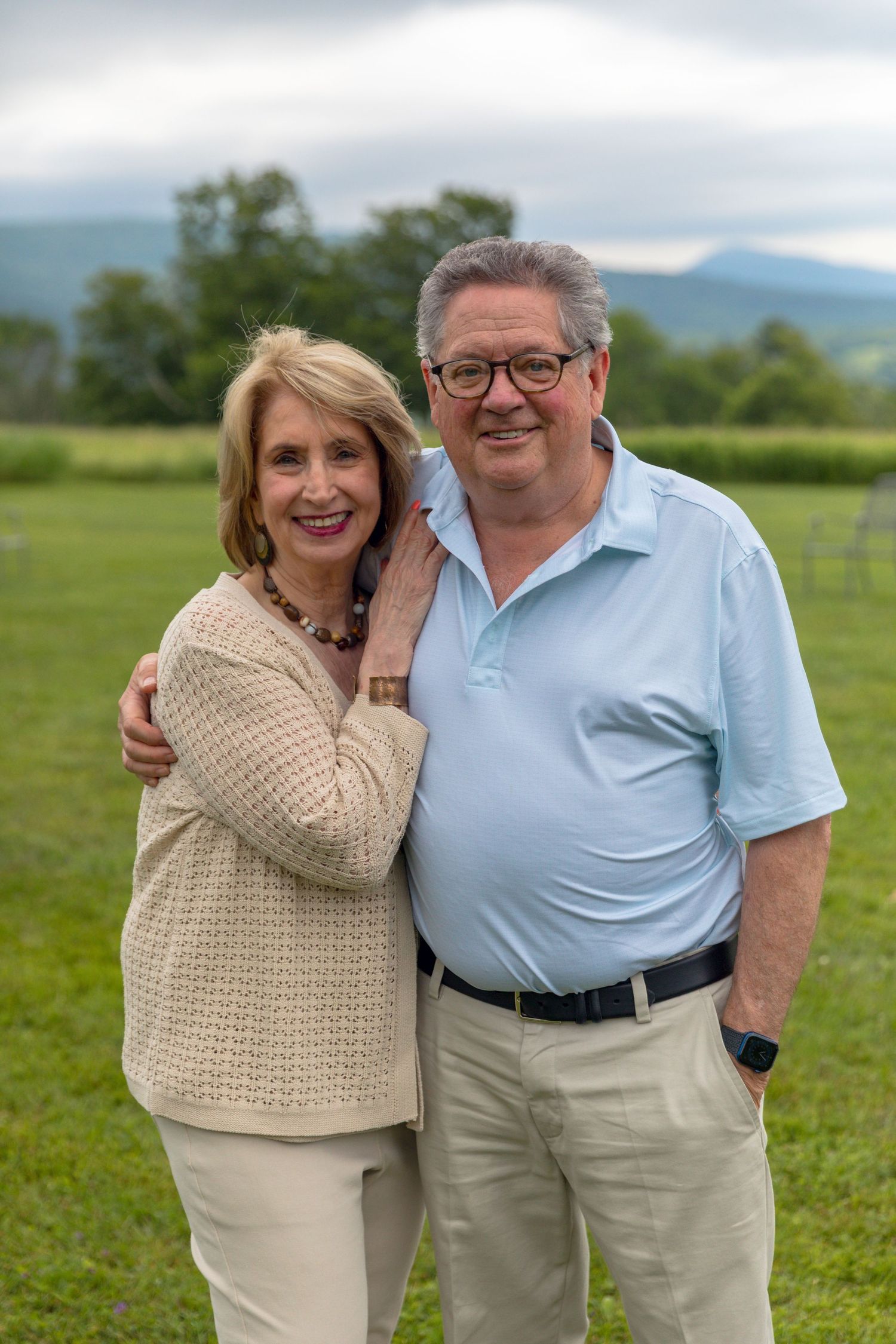 A couple embraces while standing in a grassy field wearing coordinated light-colored outfits.