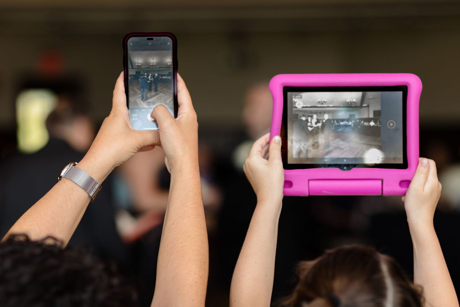 Multiple hands holding up phones and tablets to record a special moment at an event.