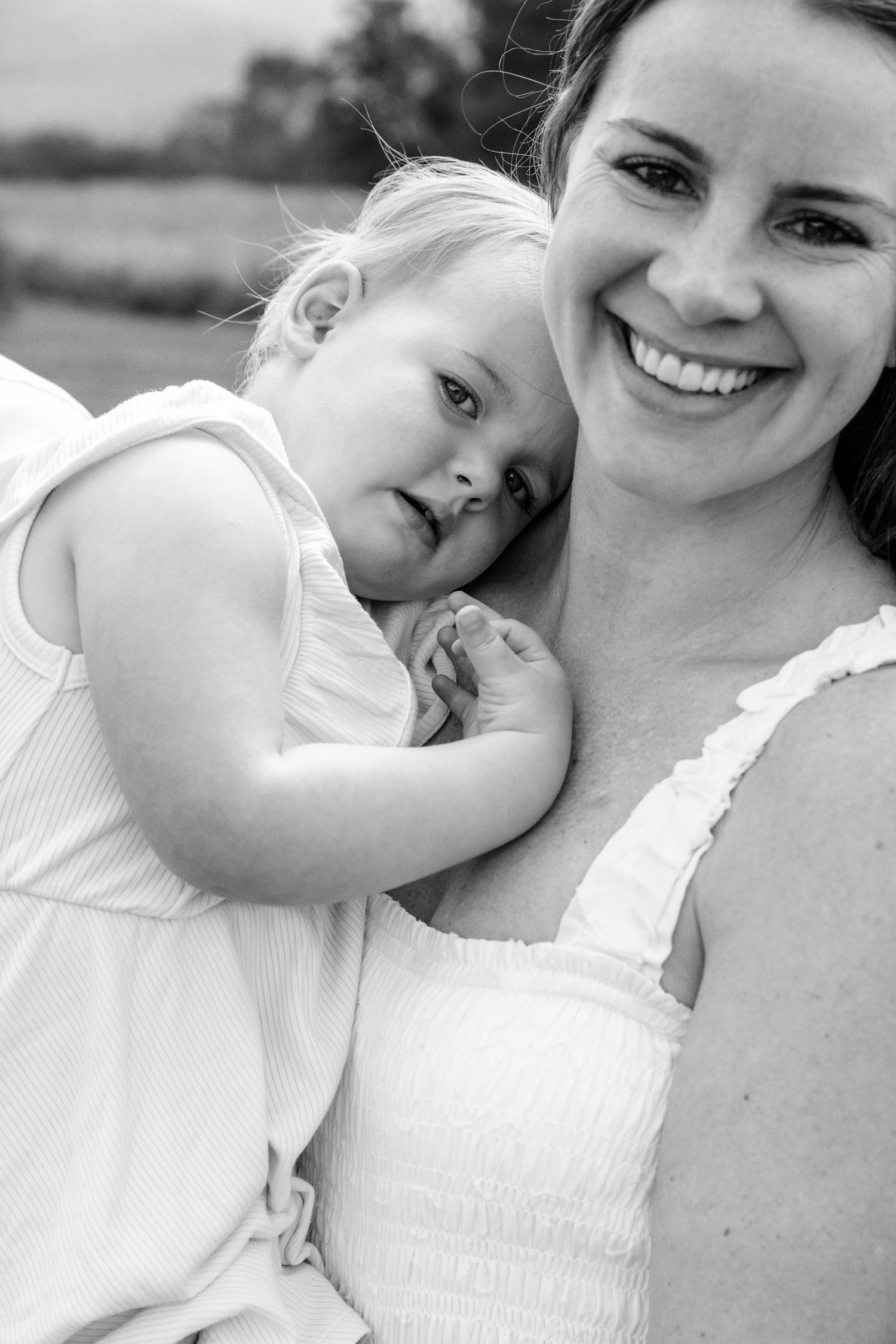 A tender black and white portrait of a parent and child in white summer clothing.