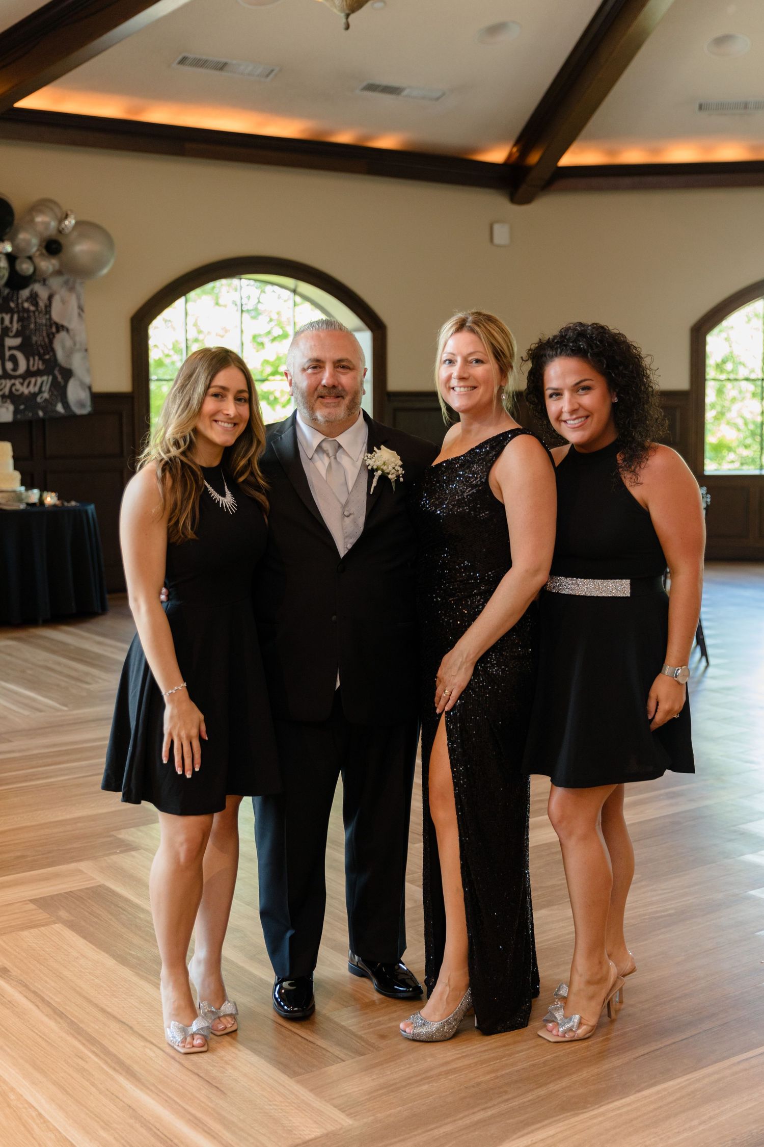 A group poses together in formal black attire on a polished wood floor at an elegant event venue.