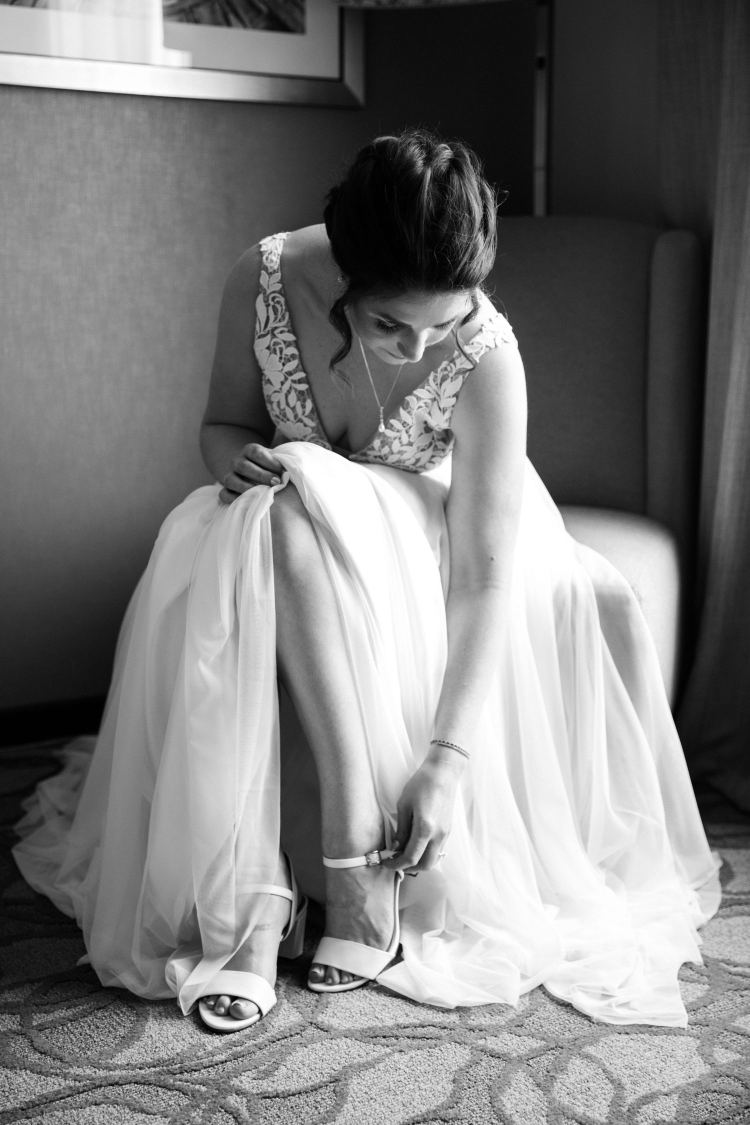 Artistic black and white detail shot of wedding dress hem and shoes on textured carpet.