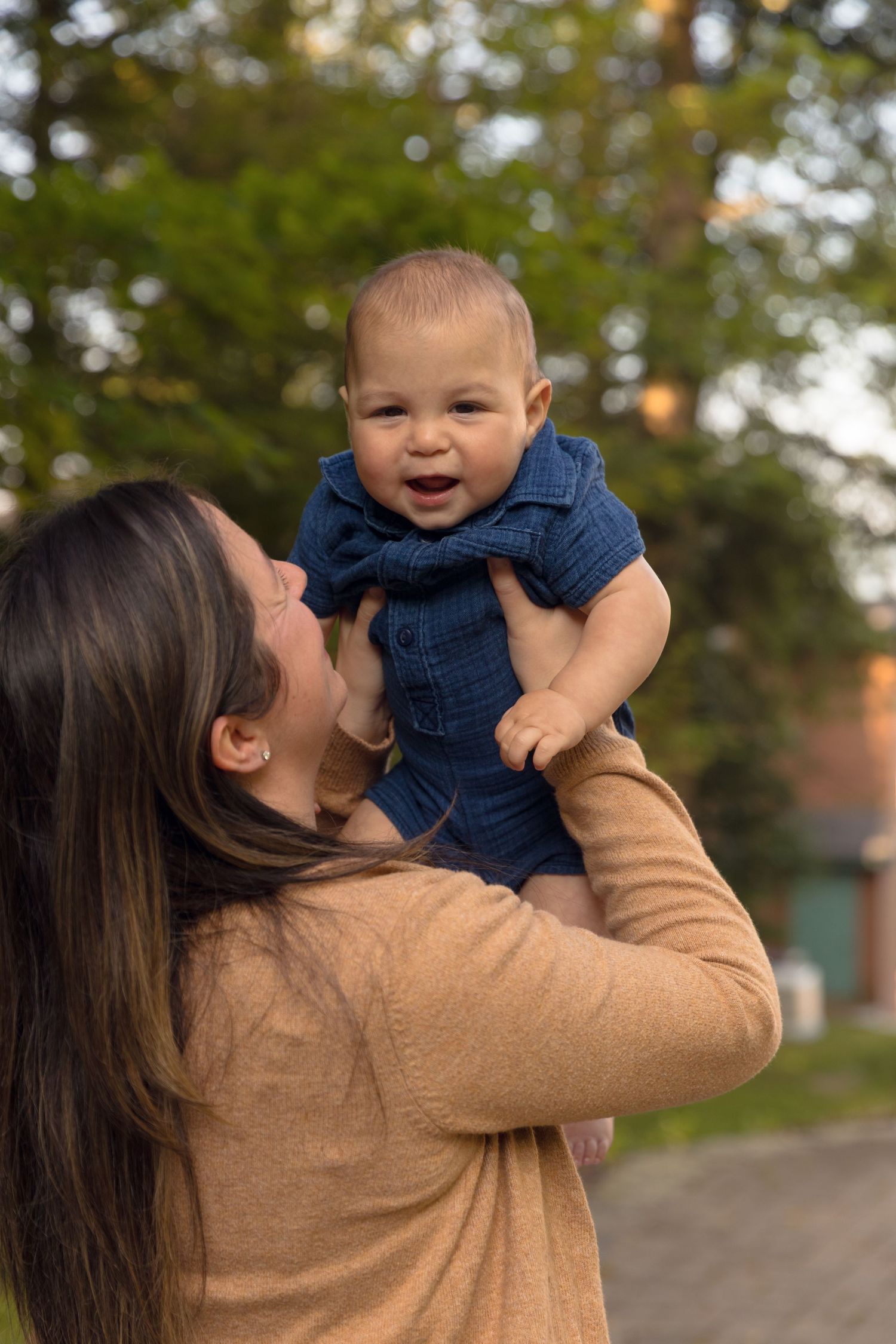 A joyful moment captured between parent and baby against an outdoor autumn backdrop.