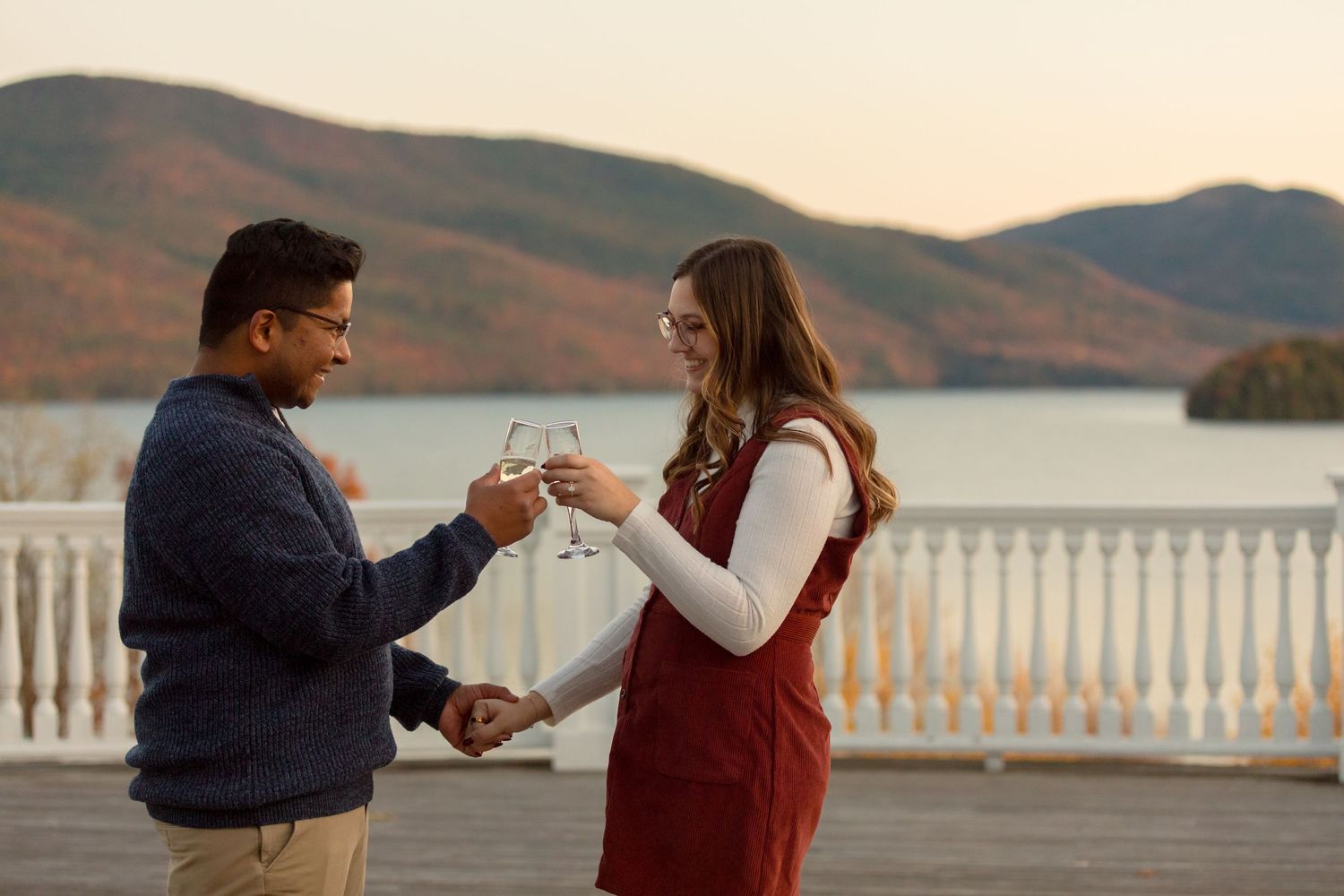 Couple toasting with wine glasses against a scenic mountain and lake backdrop.