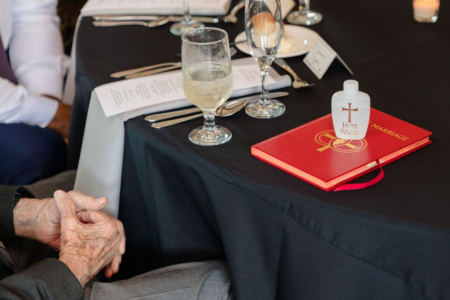 Table settings with glasses and red books on black tablecloths at a formal event.