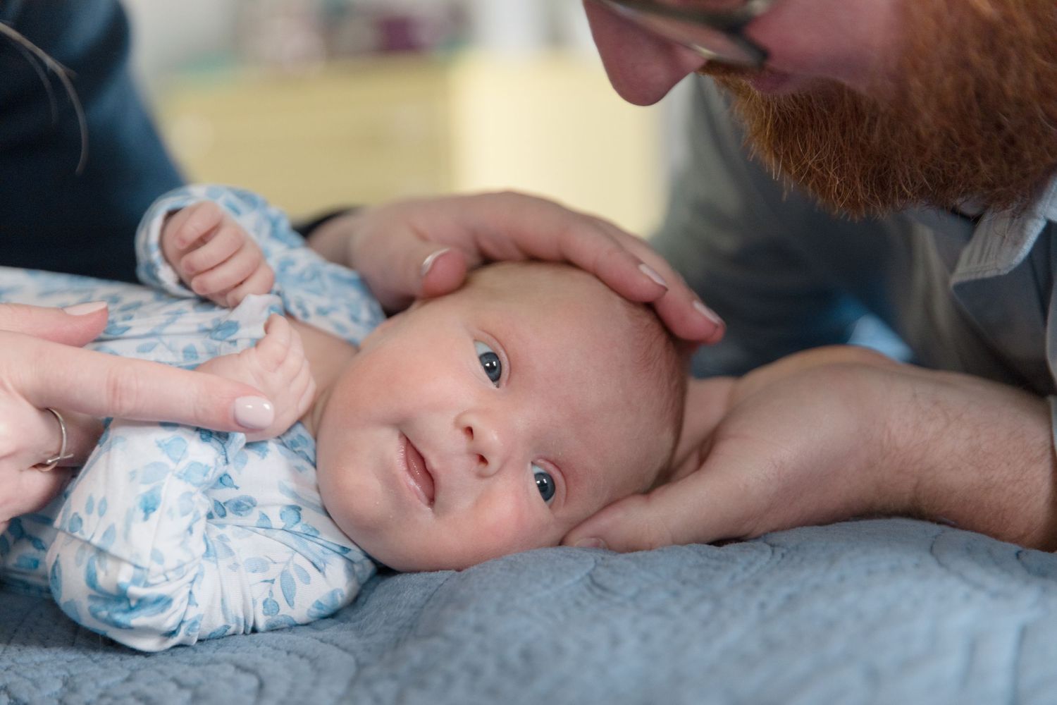Close-up of a baby in blue clothing being gently touched by caring hands.
