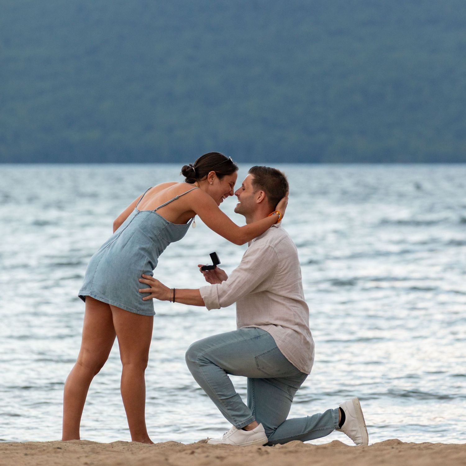 A romantic beach proposal scene at sunset with the lake waves in the background.